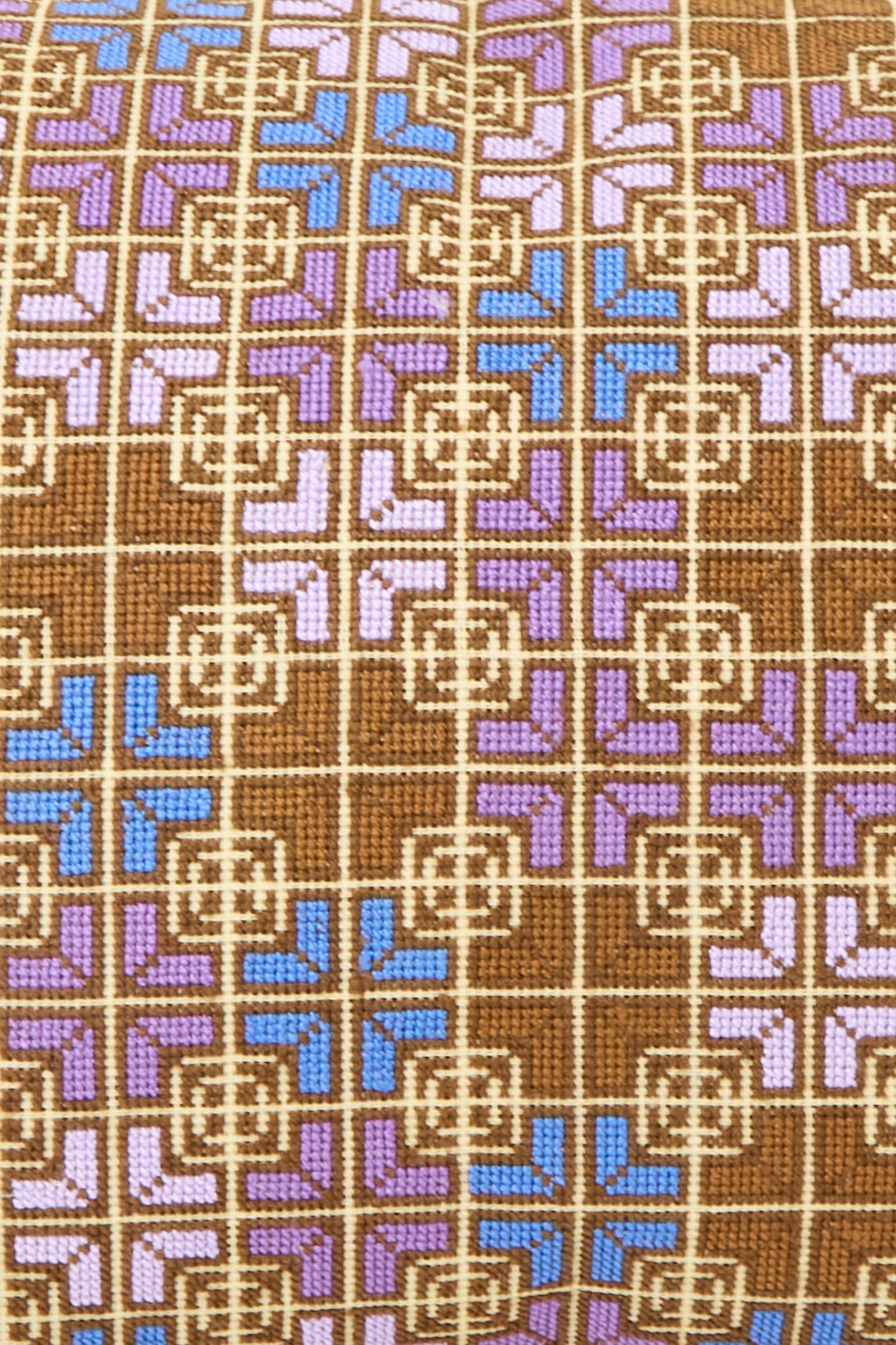 A close-up of the Kissweh Rana Hand Embroidered Pillow in Lilac and Cognac, featuring a Belgian linen cover with a geometric pattern of interlocking squares and lines in brown, beige, purple, and blue.