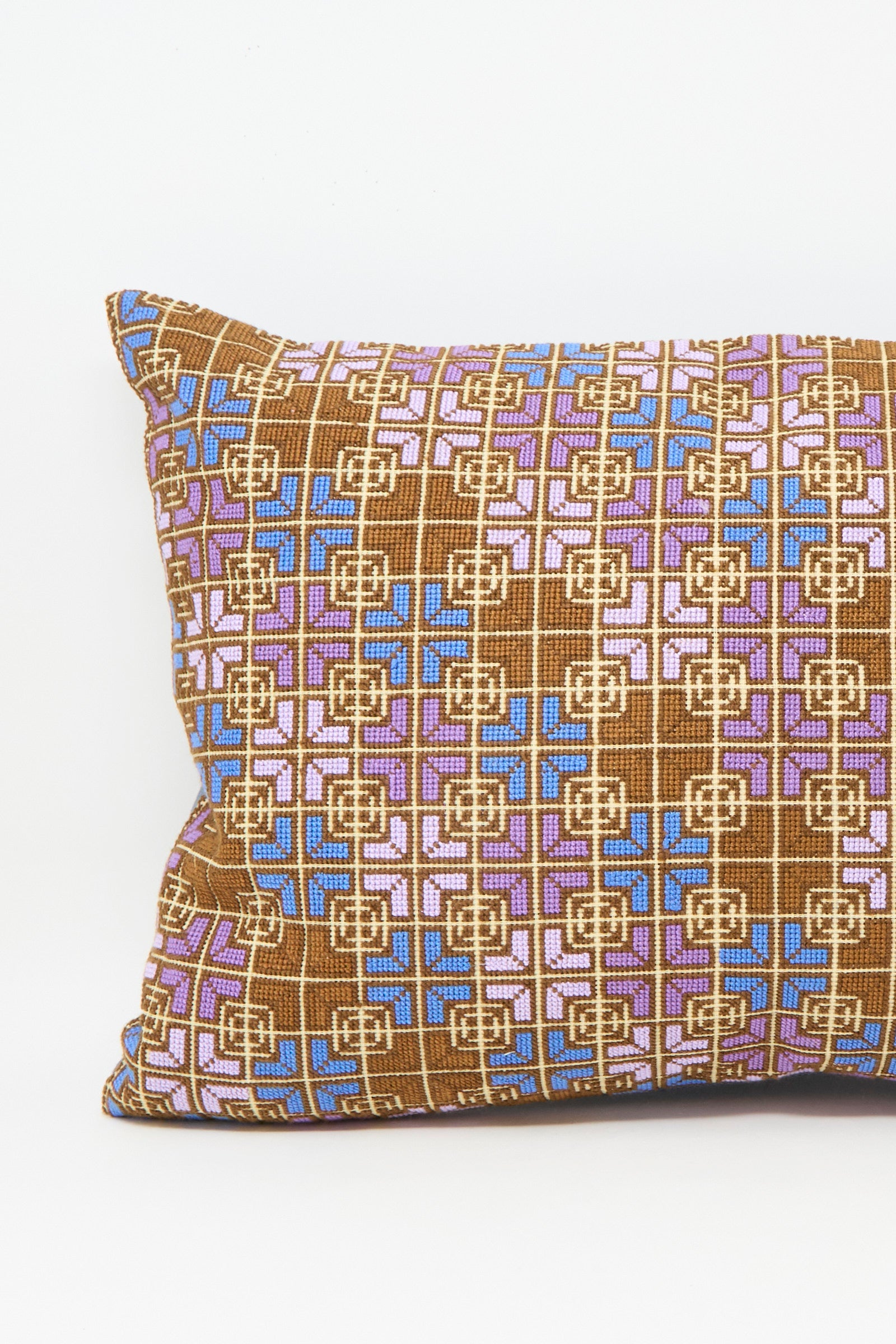 The Rana Hand Embroidered Pillow in Lilac and Cognac by Kissweh features a rectangular design with a geometric pattern in brown, pink, purple, and blue on a white background.