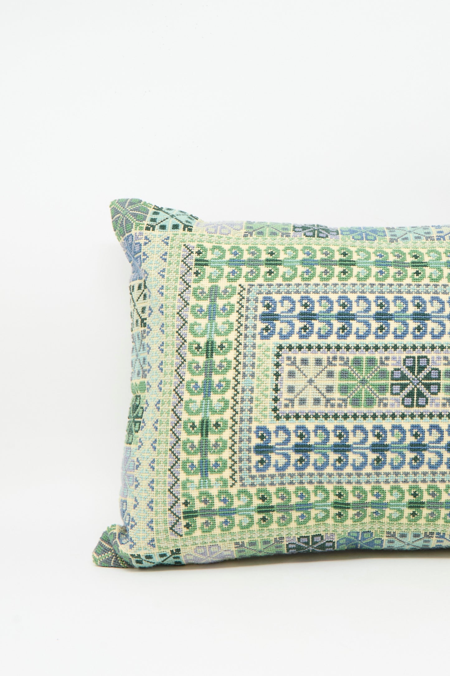The Yasmin Hand Embroidered Pillow in Olive by Kissweh features a geometric design in green, blue, and black on Belgian linen with a white background. It is shown resting against a plain white surface.