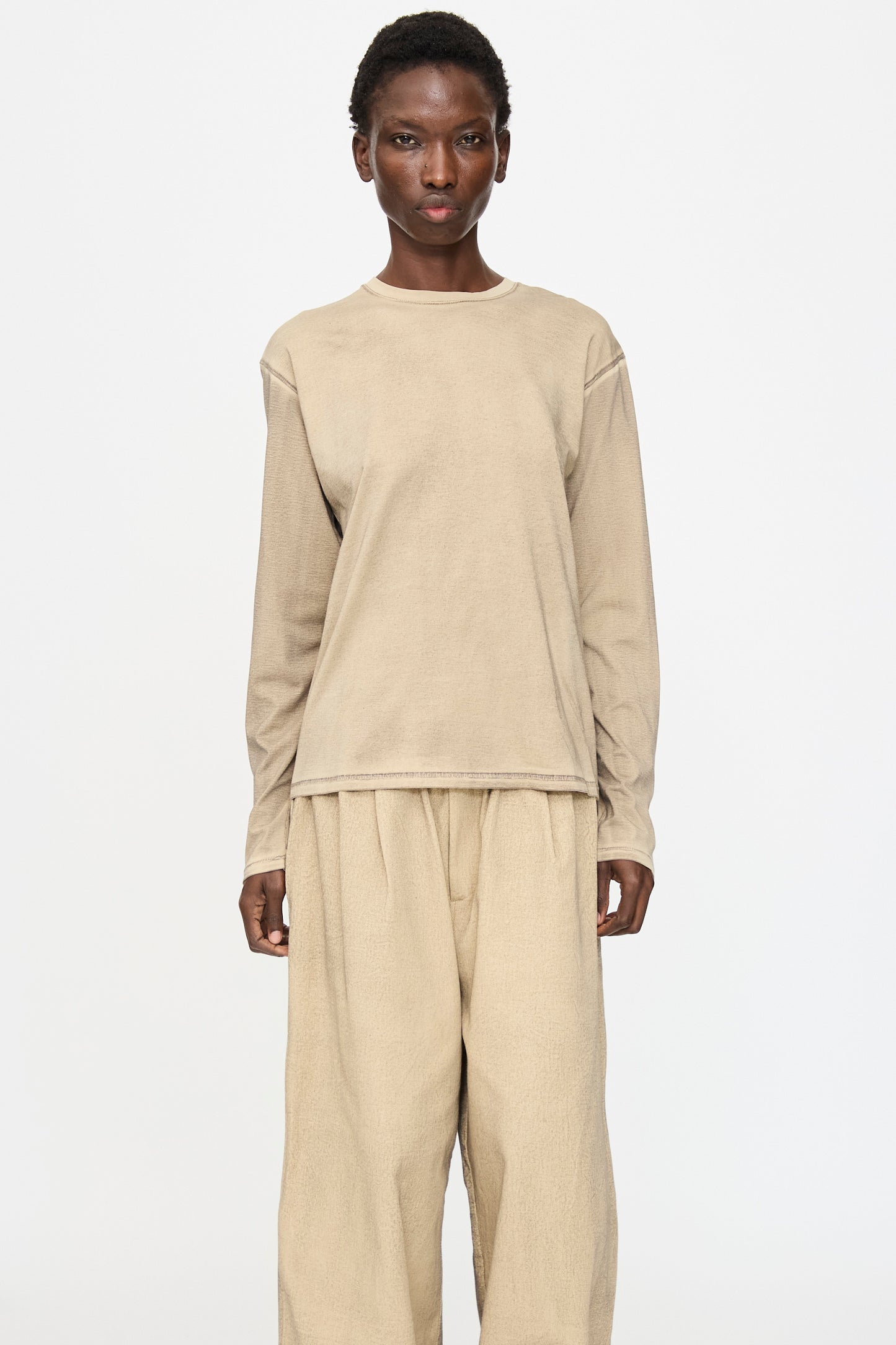 Person standing against a plain white background, wearing the Lauren Manoogian Bias Long Sleeve Tee in Painted Antique and matching wide-legged pants.