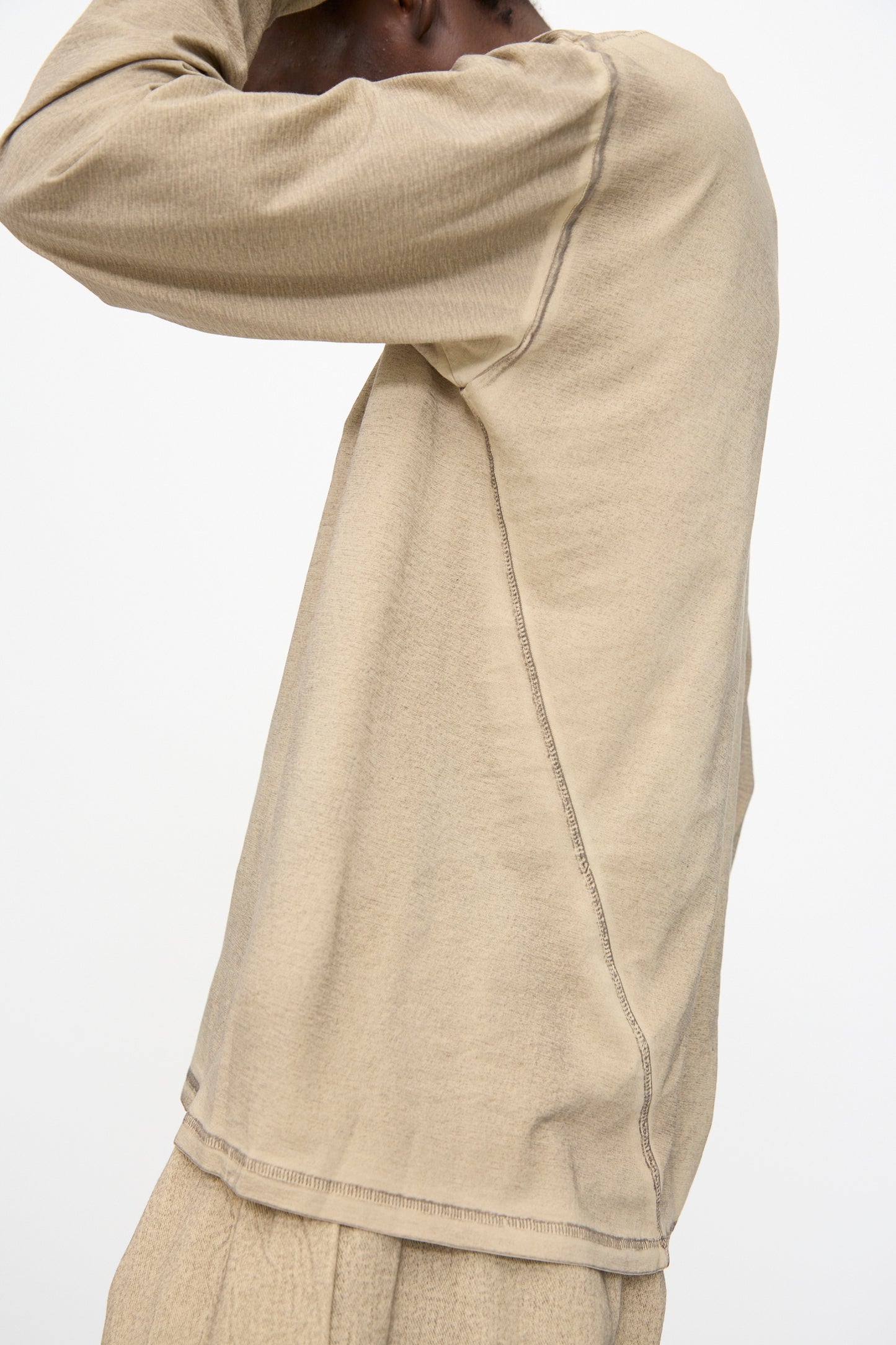 A person wears the Lauren Manoogian Bias Long Sleeve Tee in Painted Antique with matching pants, hands raised near their head, against a plain light background.