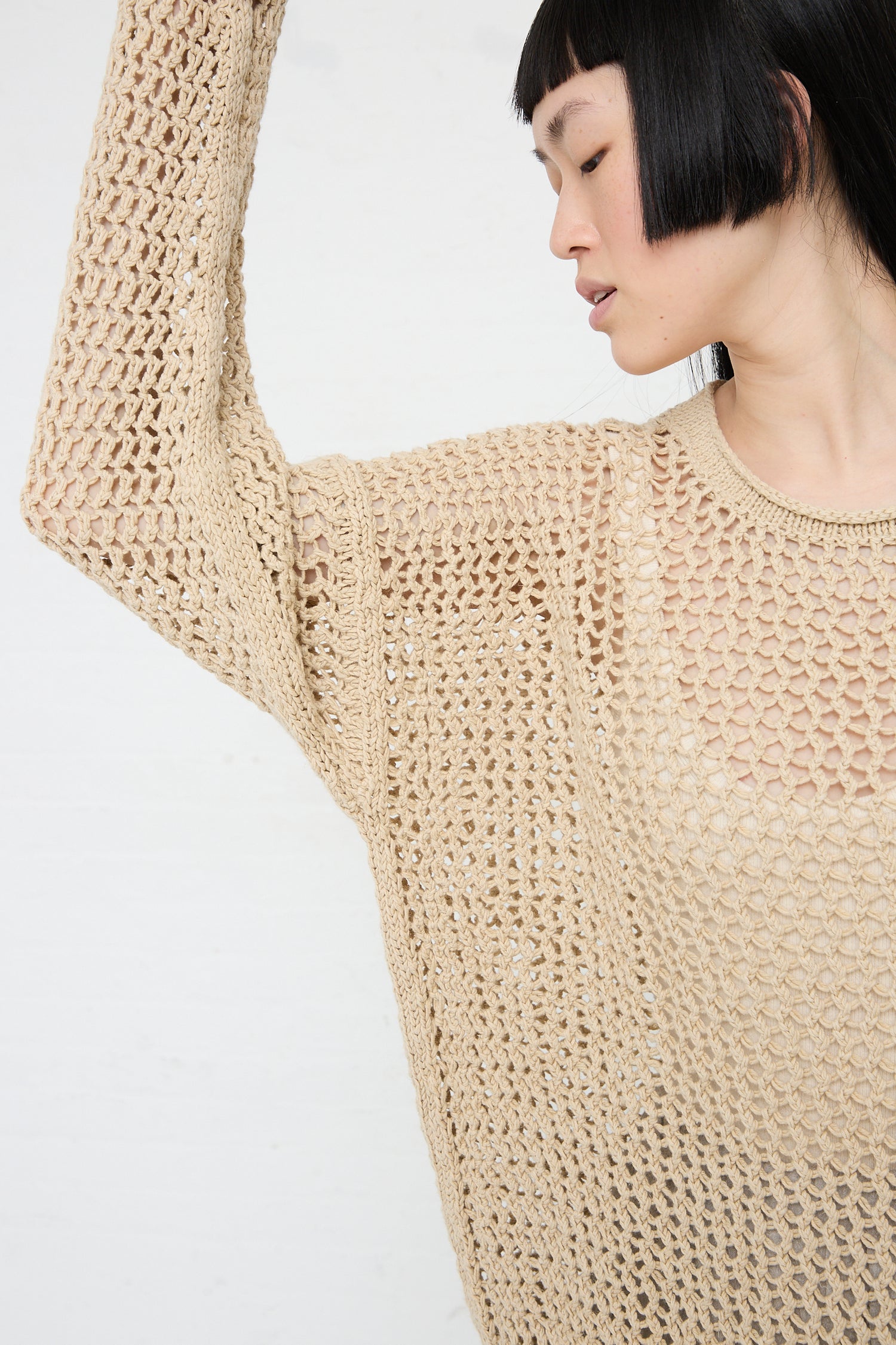 A person in a Lauren Manoogian Big Net Pullover in Jute raising their arm, displaying the sweater's texture.