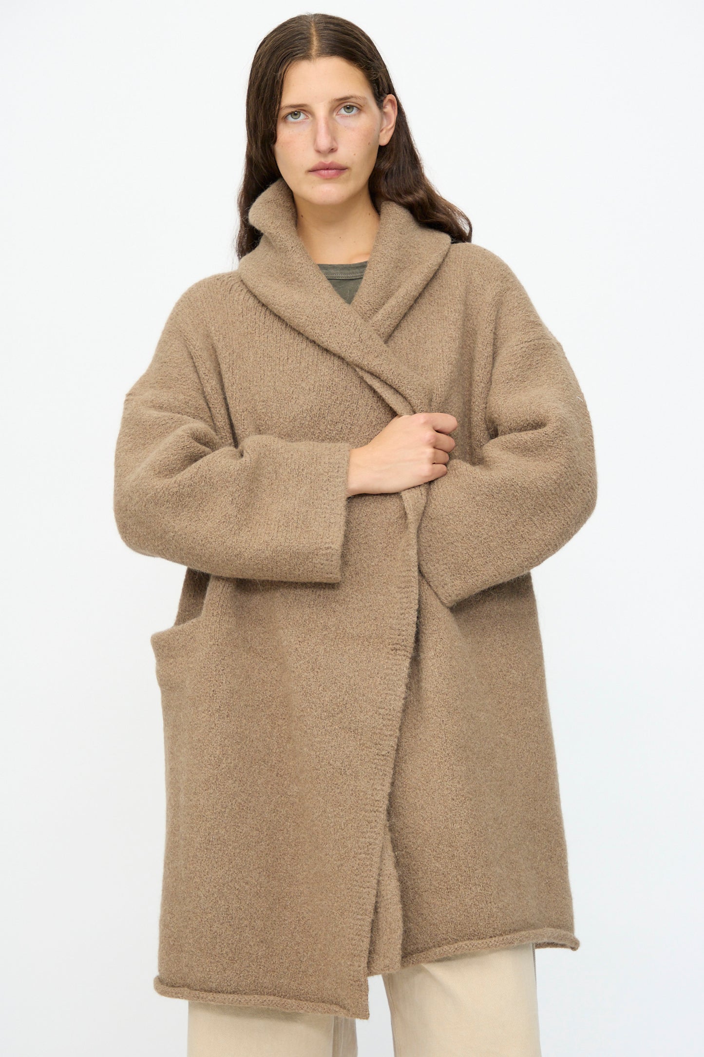 A person wears the Lauren Manoogian Capote Coat in Tobacco, a relaxed fit alpaca wool coat with large front pockets, standing against a plain white background.