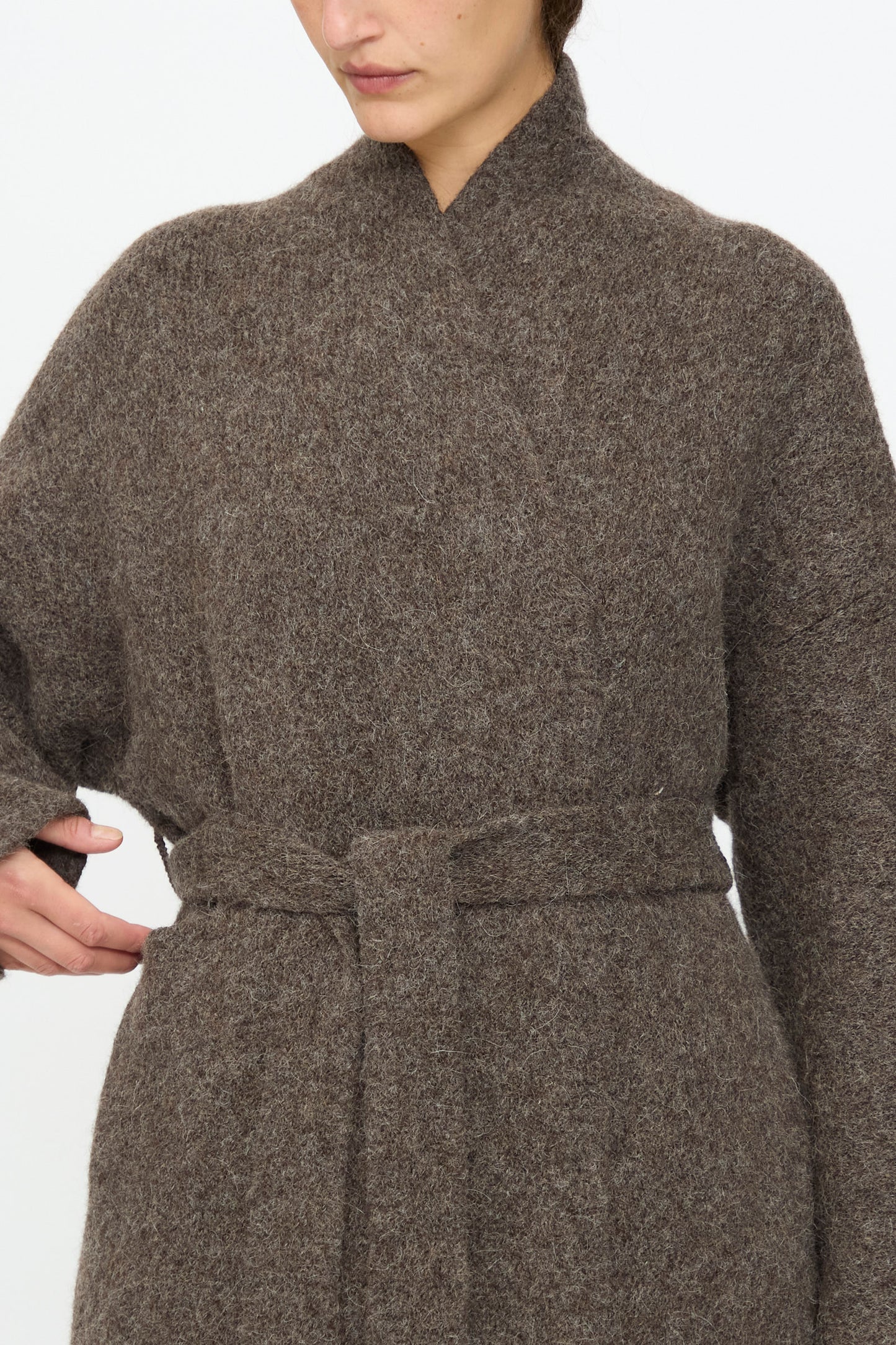 Model wears the Lauren Manoogian Coto Cardigan in Patina, a brown belted knit with a relaxed fit and textured finish, shown from shoulders to mid-thigh with one hand resting on the belt.
