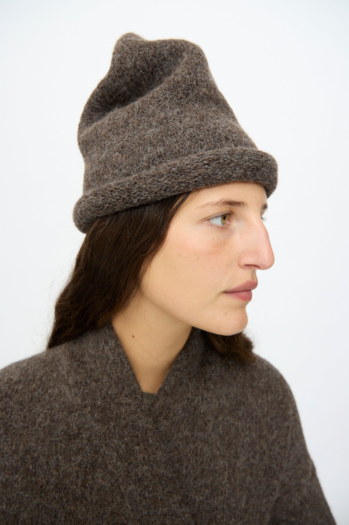 Person wearing the Lauren Manoogian Crown Beanie in Patina and a textured brown knit sweater, facing left against a plain white background.