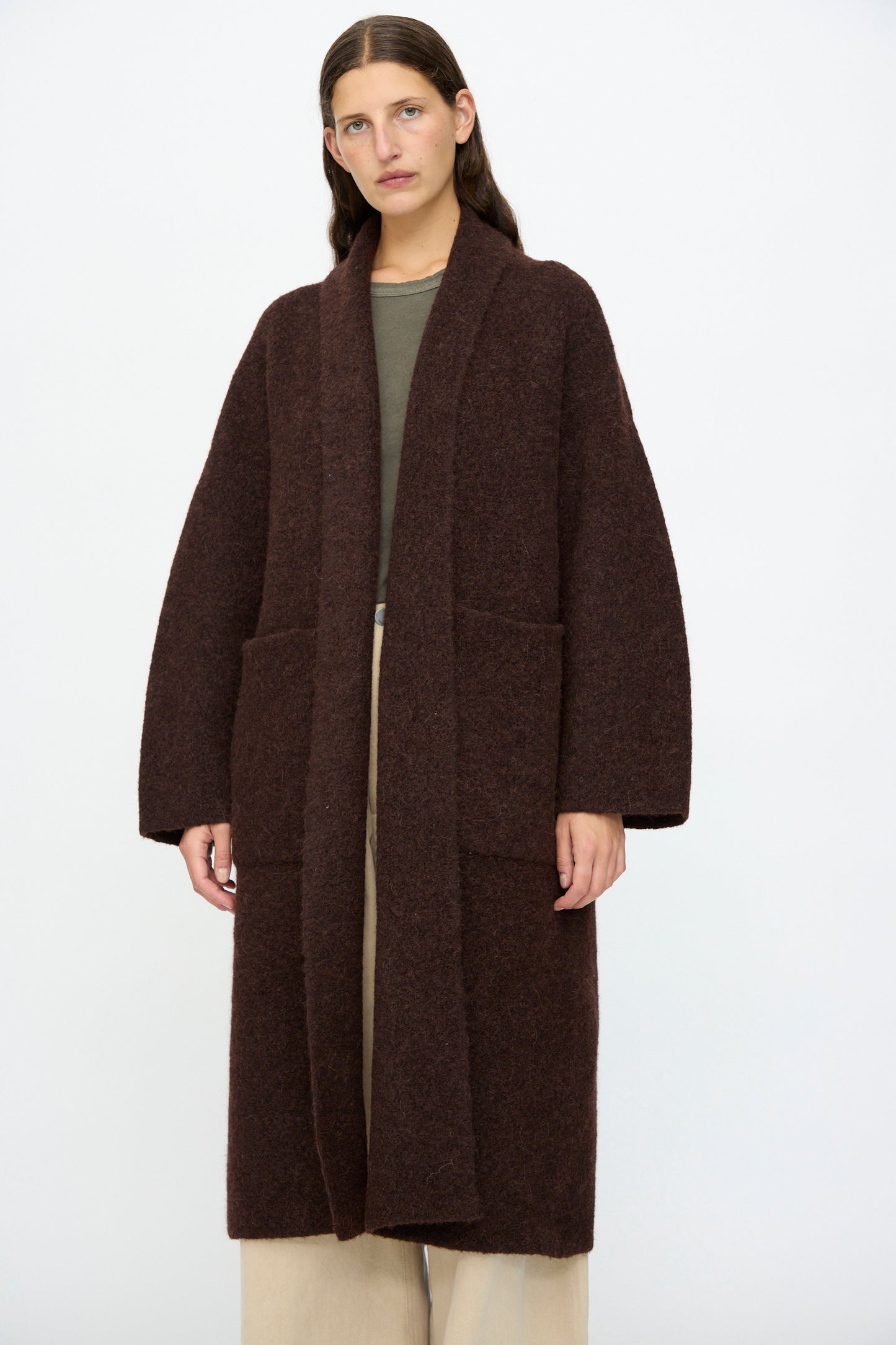 A person wears the Lauren Manoogian Double Face Long Coat in Merlot over a greenish top and beige wide-leg pants, standing against a plain white background.