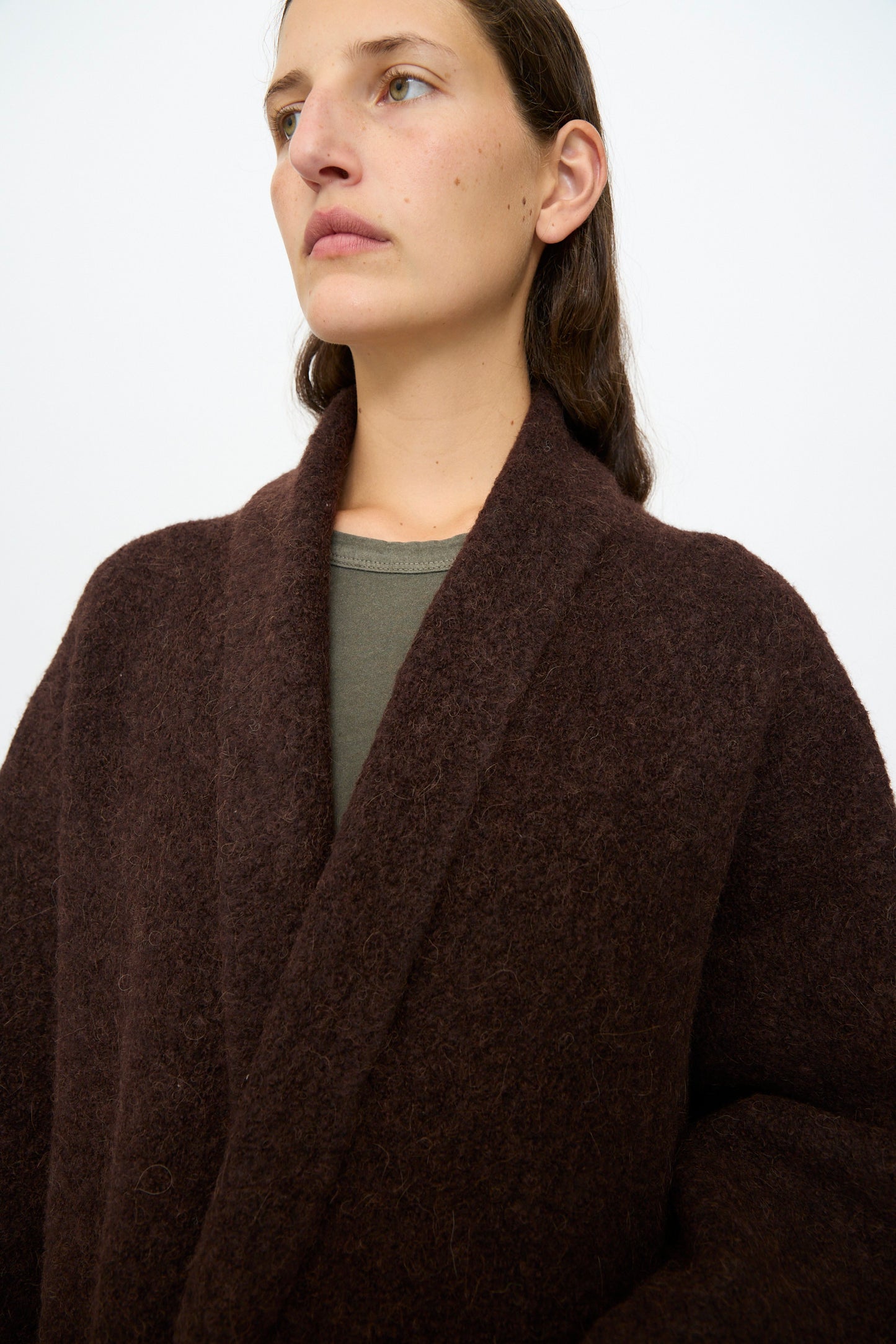 A woman with straight brown hair wears the Lauren Manoogian Double Face Long Coat in Merlot over a green top, standing against a plain light background.