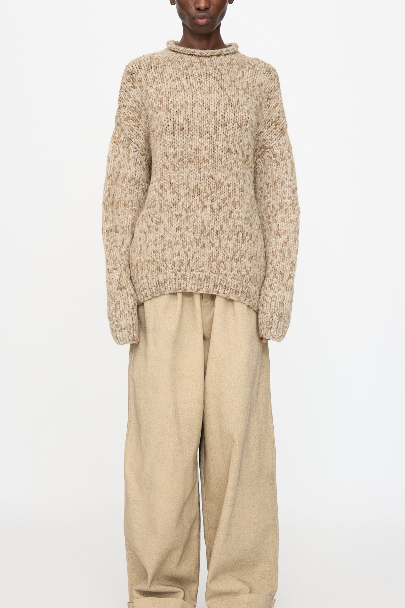 A person wears the Lauren Manoogian Handknit Paint Rollneck in Tobacco with wide-legged light brown pants, standing against a plain white background.