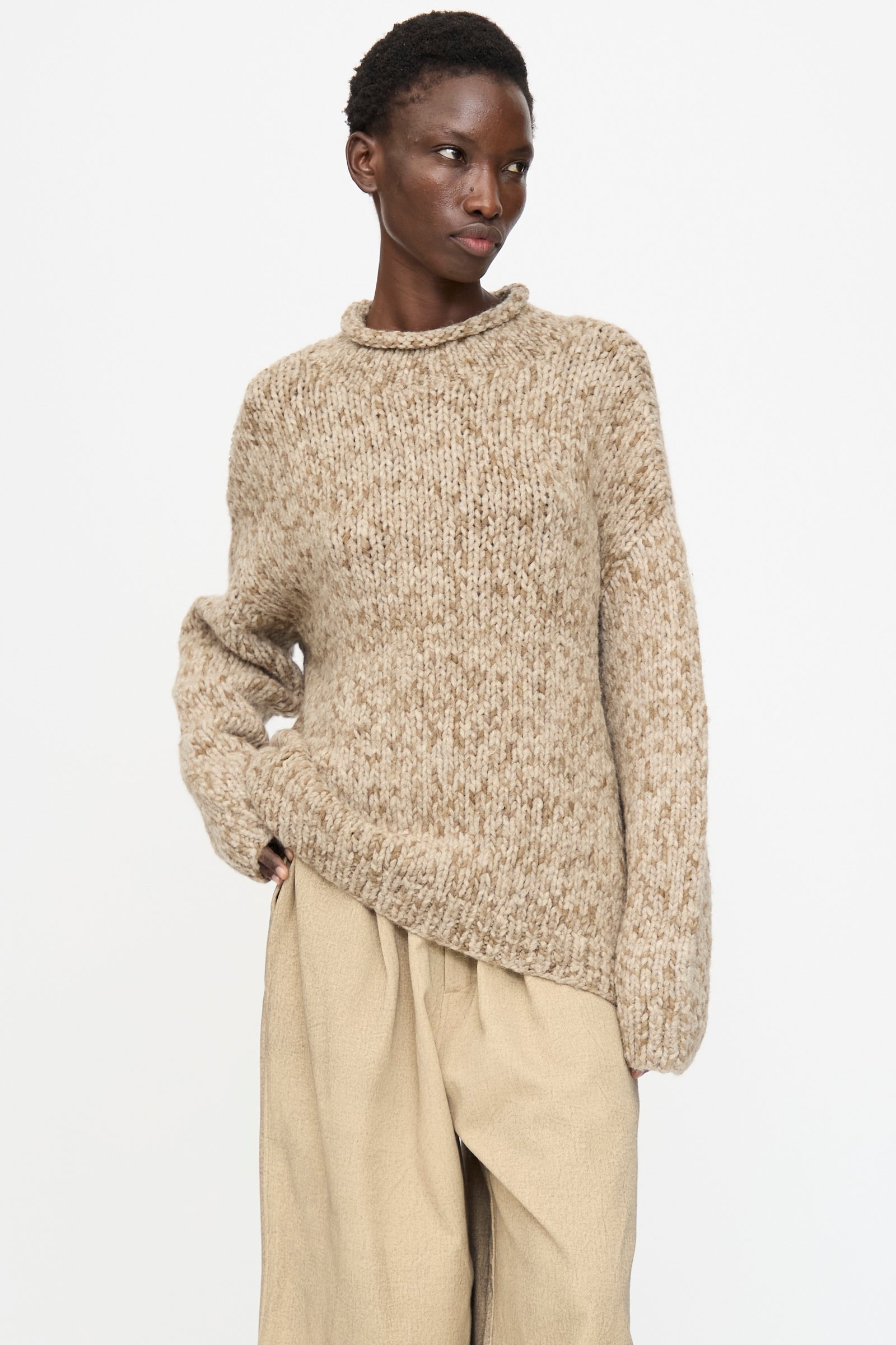 A person wears the Lauren Manoogian Handknit Paint Rollneck in Tobacco with loose light tan pants, standing against a plain white background.