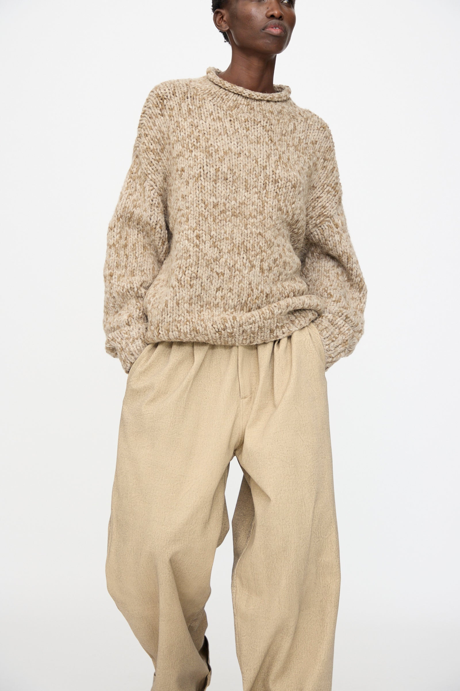 A person wearing the Lauren Manoogian Handknit Paint Rollneck in Tobacco and loose beige pants stands against a plain white background.