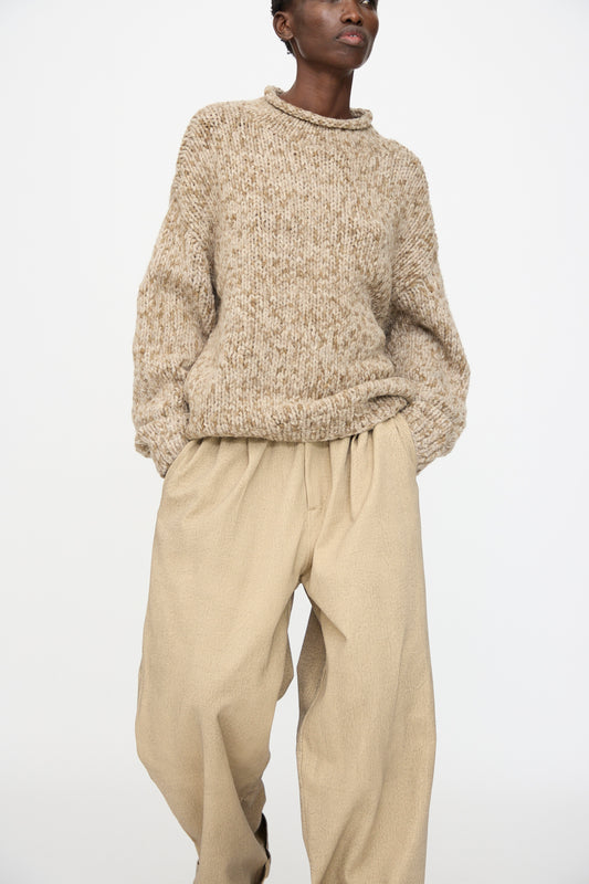 A person wearing the Lauren Manoogian Handknit Paint Rollneck in Tobacco and loose beige pants stands against a plain white background.