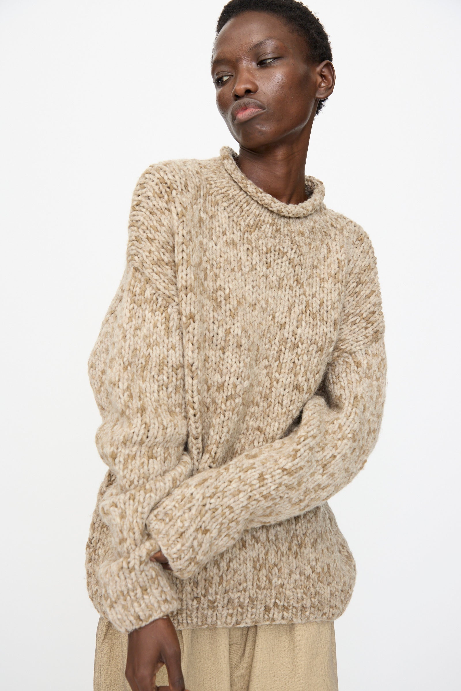 A person wears the Lauren Manoogian Handknit Paint Rollneck in Tobacco and light pants, standing against a plain white background.