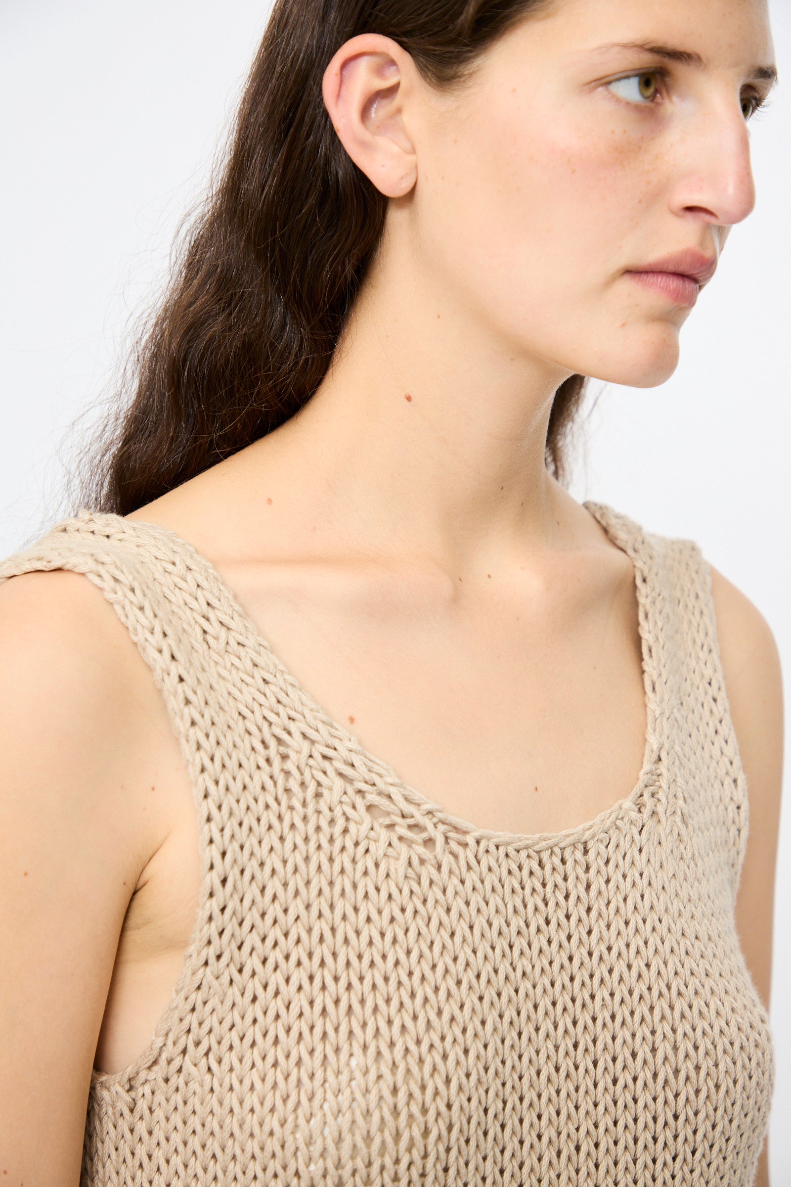 A person with long brown hair models the Lauren Manoogian Handknit Ruffle Tank in Sisal, a relaxed fit beige top, shown from the shoulders up against a plain background.