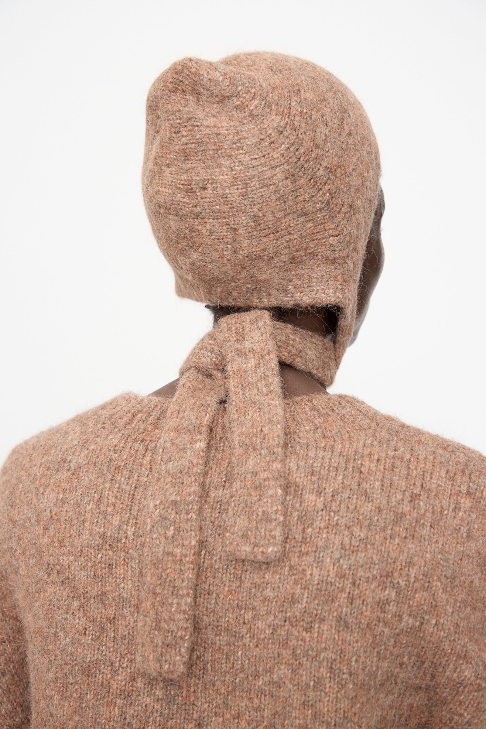 A person wearing the Lauren Manoogian Loft Bonnet in Spice, a textured brown fitted bonnet tied at the back, along with a matching brown knit sweater, shown from behind against a plain white background.