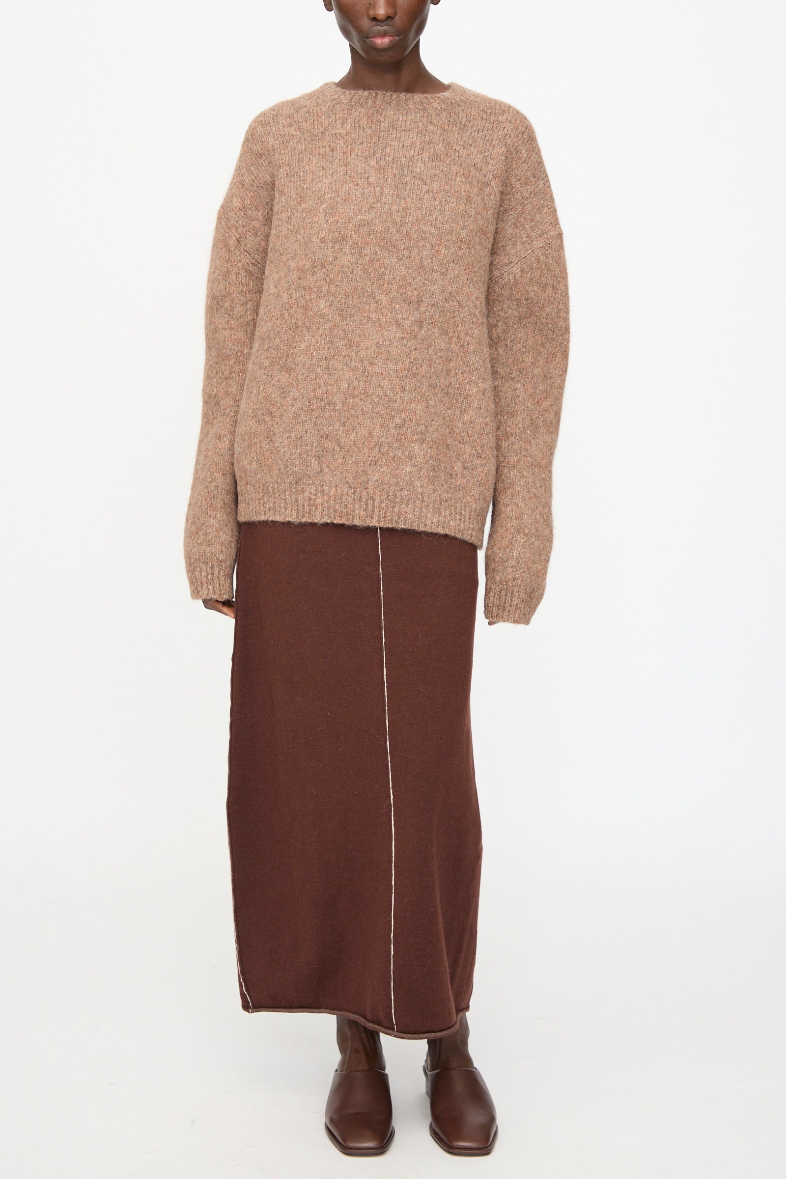 Model wears the Lauren Manoogian Loft Crewneck in Spice, paired with a long brown skirt featuring a vertical seam and brown ankle boots, standing against a plain white background.