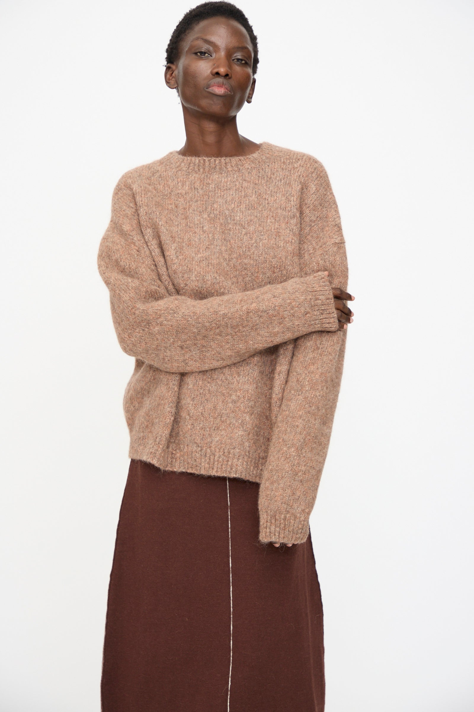 Person stands against a plain background, wearing the Lauren Manoogian Loft Crewneck in Spice and a brown skirt, arms loosely crossed.
