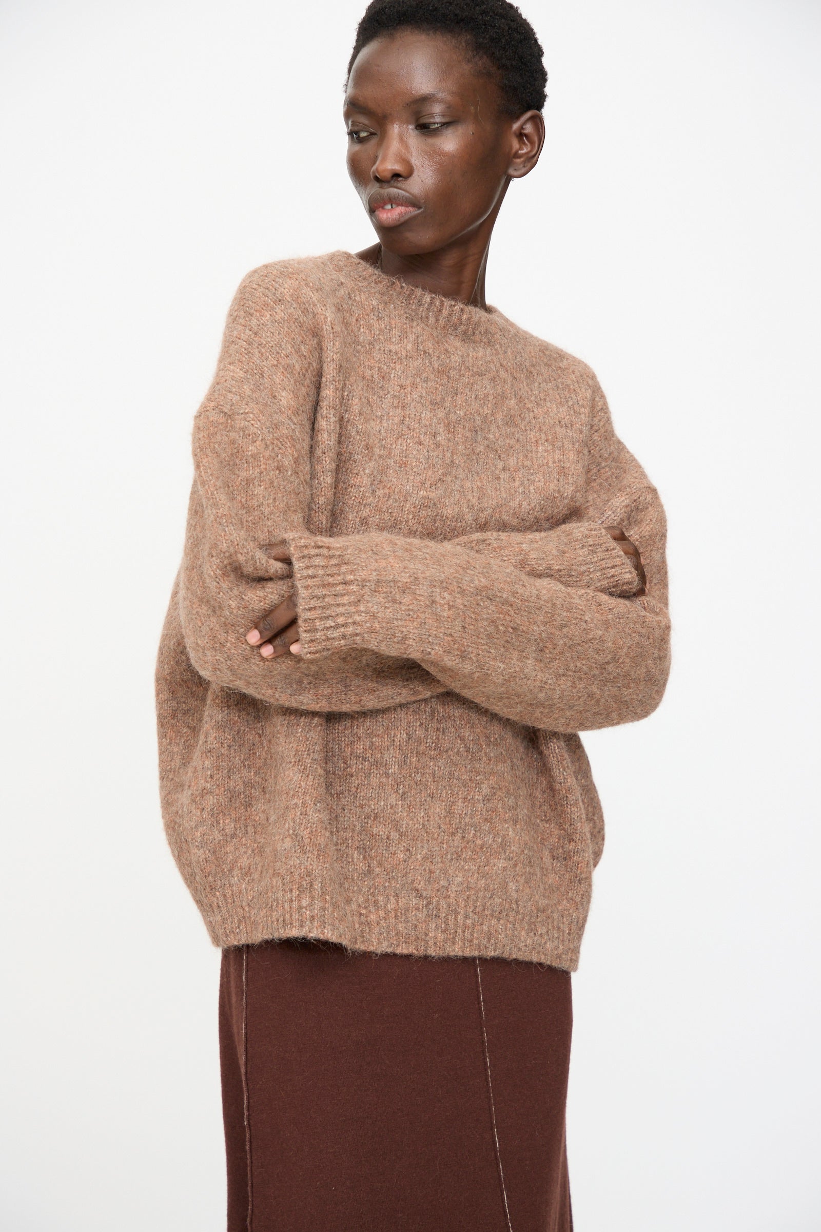 Model wears the Lauren Manoogian Loft Crewneck in Spice with a matching skirt, standing with arms crossed against a plain white background.