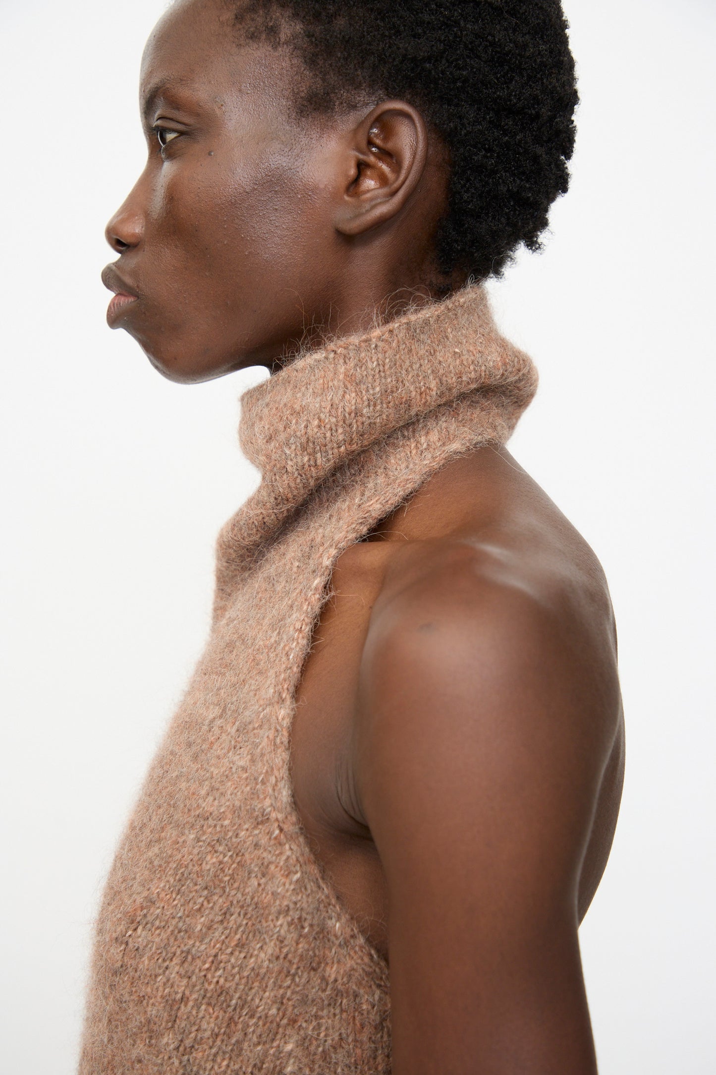 A person in profile wears the Lauren Manoogian Loft Halter in Spice, a sleeveless alpaca blend turtleneck with a textured brown finish and ribbed hem, set against a plain white background.