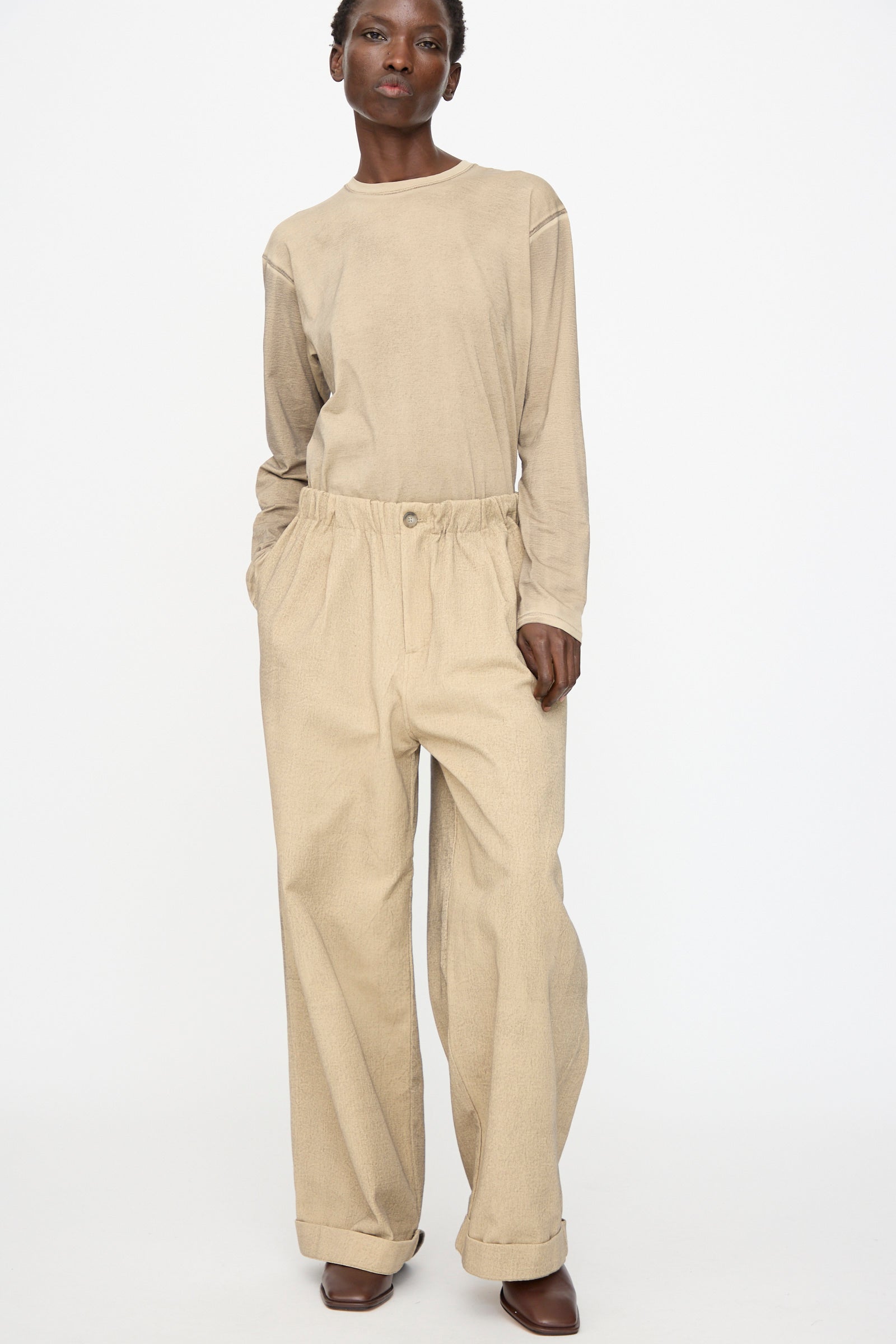 A person stands against a plain white background wearing Lauren Manoogian's oversized fit beige long-sleeve top, Painted Trouser in Antique, and brown shoes.