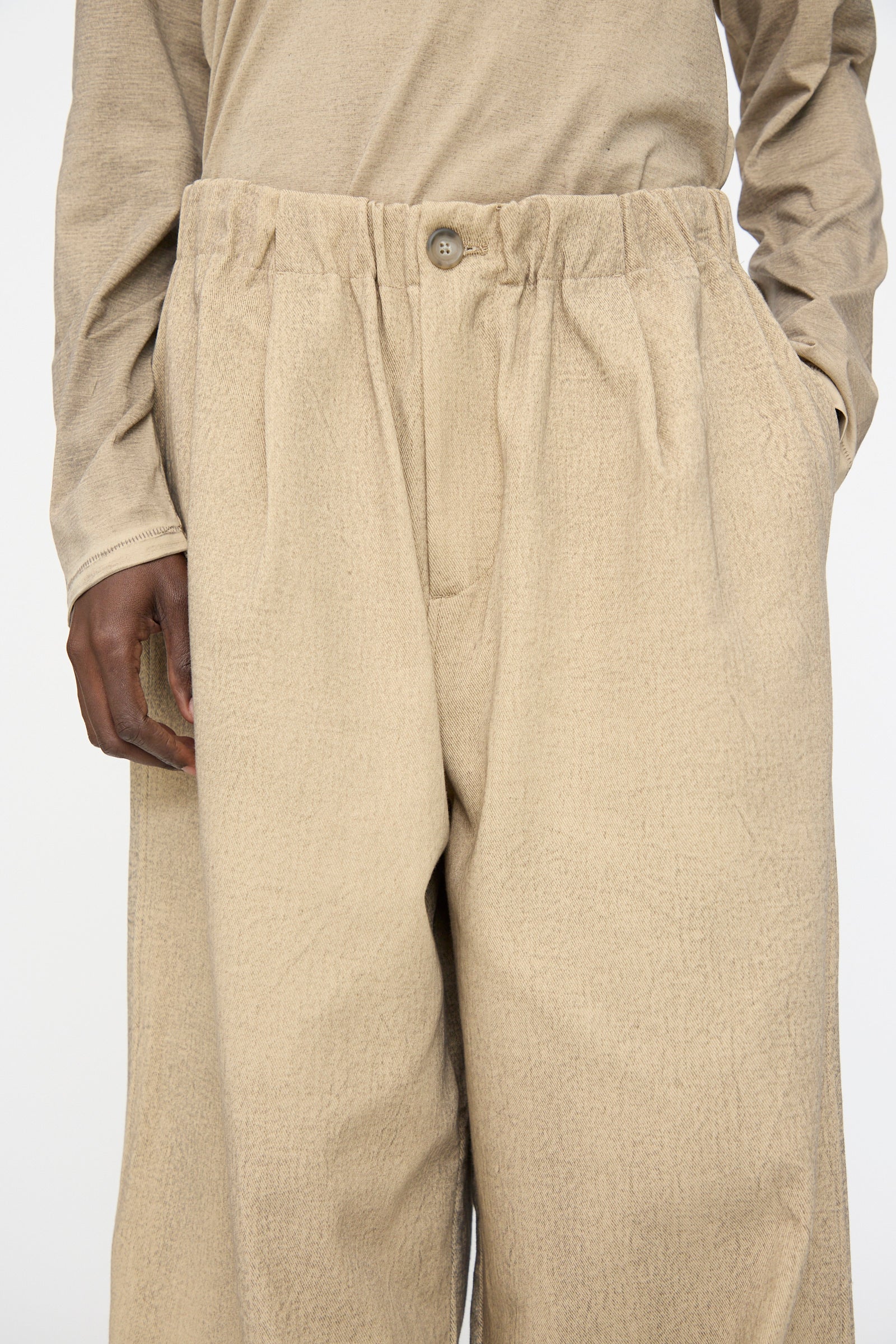 Model wears Lauren Manoogian’s Painted Trouser in Antique—loose-fitting, textured beige cotton trousers with an oversized fit—paired with a matching long-sleeve top, shown from waist to mid-thigh with one hand partly in the pocket.