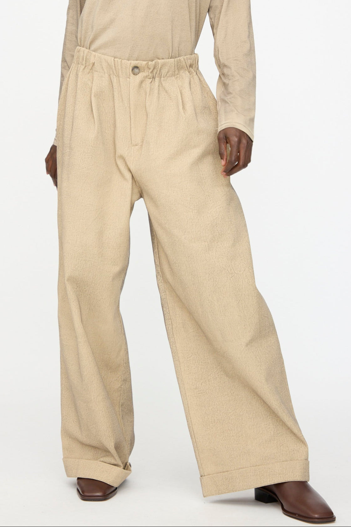 Wearing Lauren Manoogian’s Painted Trouser in Antique—loose, high-waisted cotton with button and pleats—paired with brown square-toe shoes and a beige long-sleeve top for an effortless oversized look.