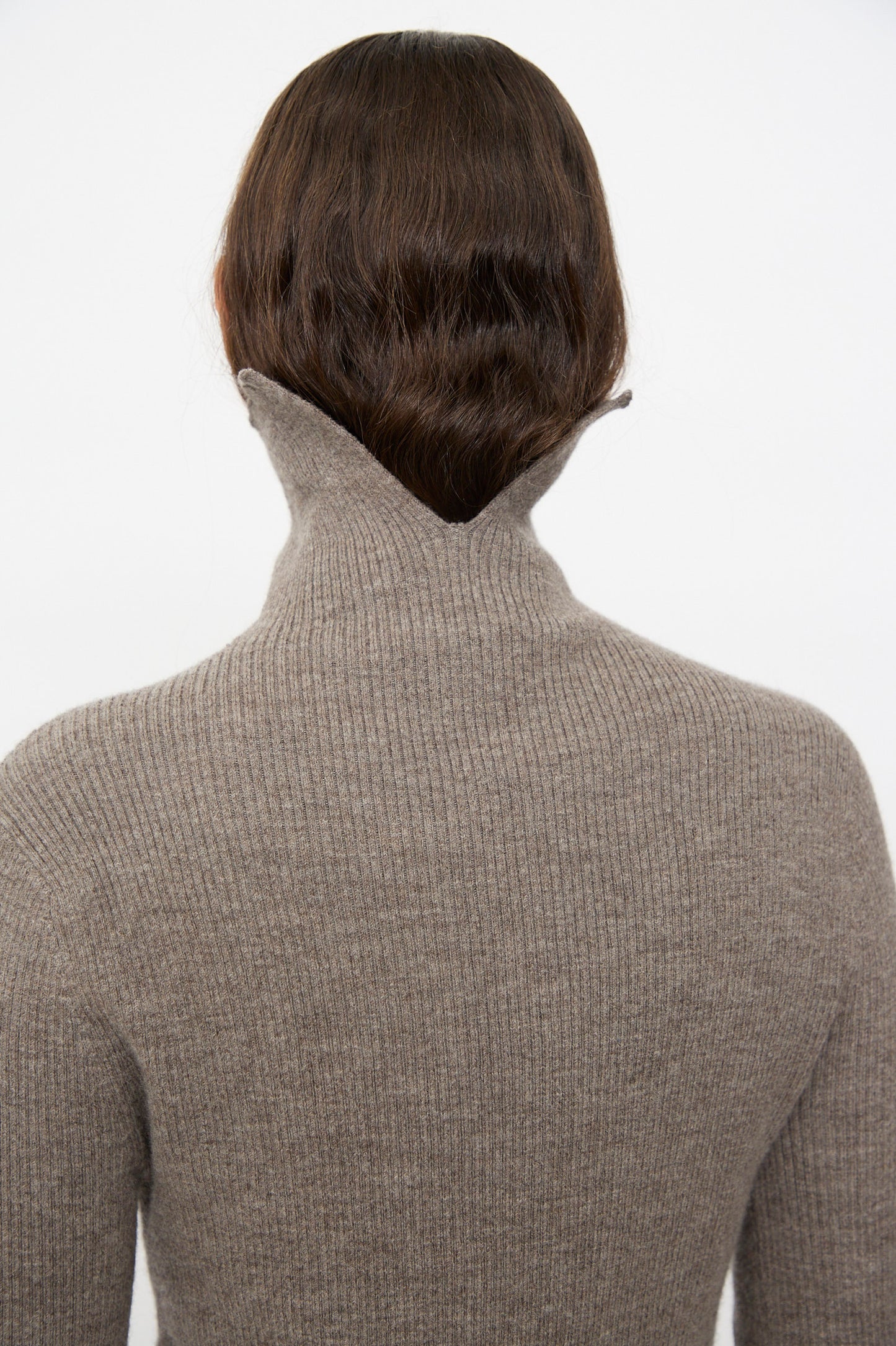 A person with long, wavy brown hair is shown from the back wearing the Lauren Manoogian Rib Split Turtleneck in Cinder, a soft merino wool sweater, against a plain background.