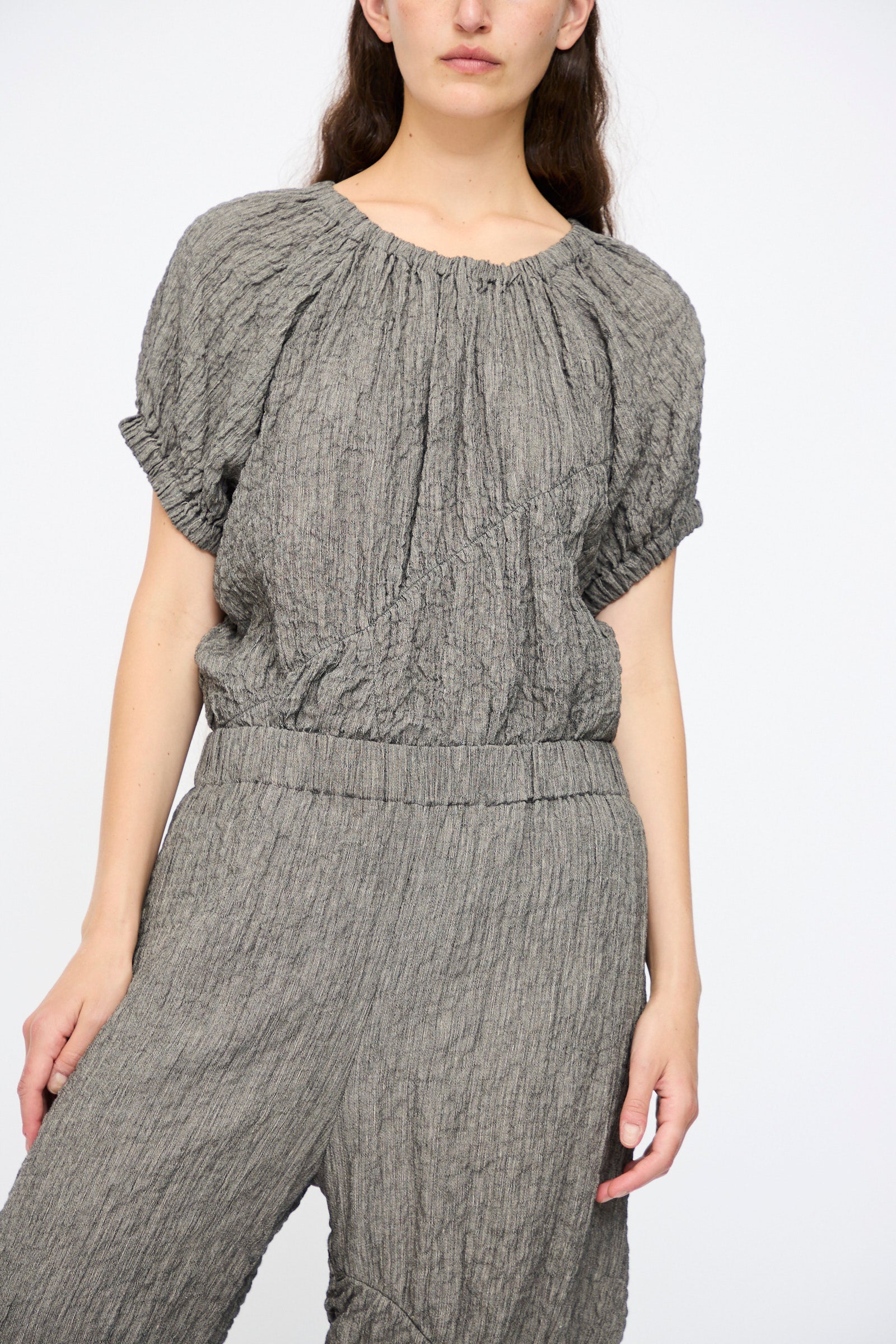 A person wears Lauren Manoogian’s Shirred Pants in Charcoal with a matching textured, relaxed fit short-sleeve top, standing against a plain white background.