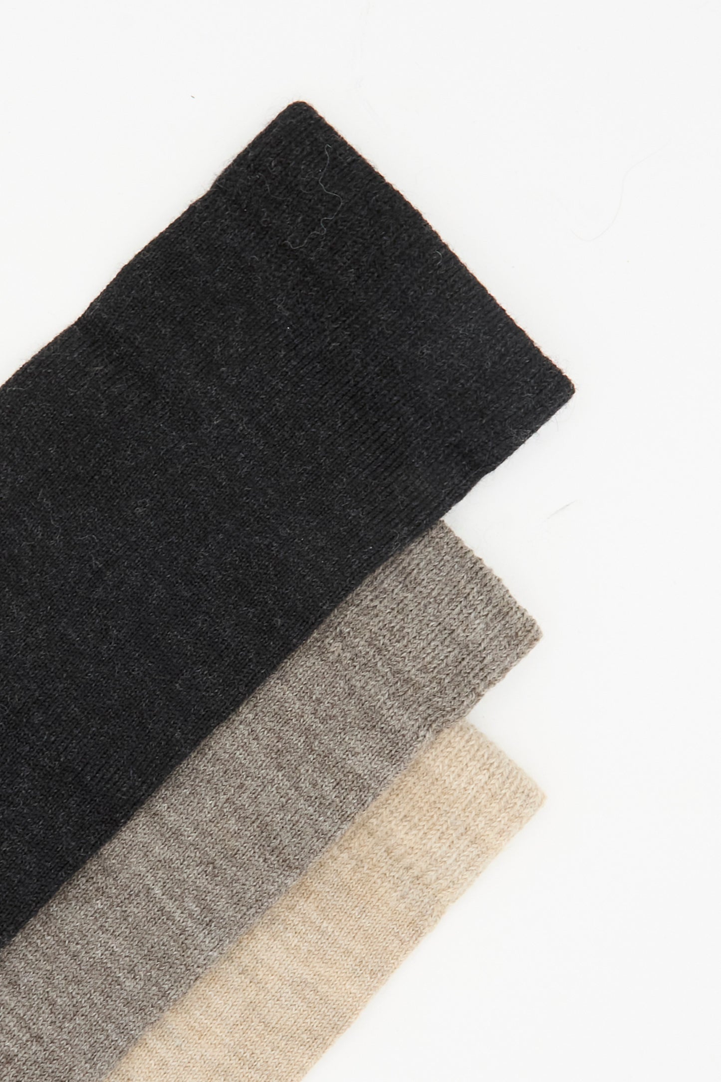 Three pairs of Lauren Manoogian's Sock Set in Mix, made from soft alpaca wool in Peru, are stacked diagonally on a white background in dark gray, light gray, and beige tones.
