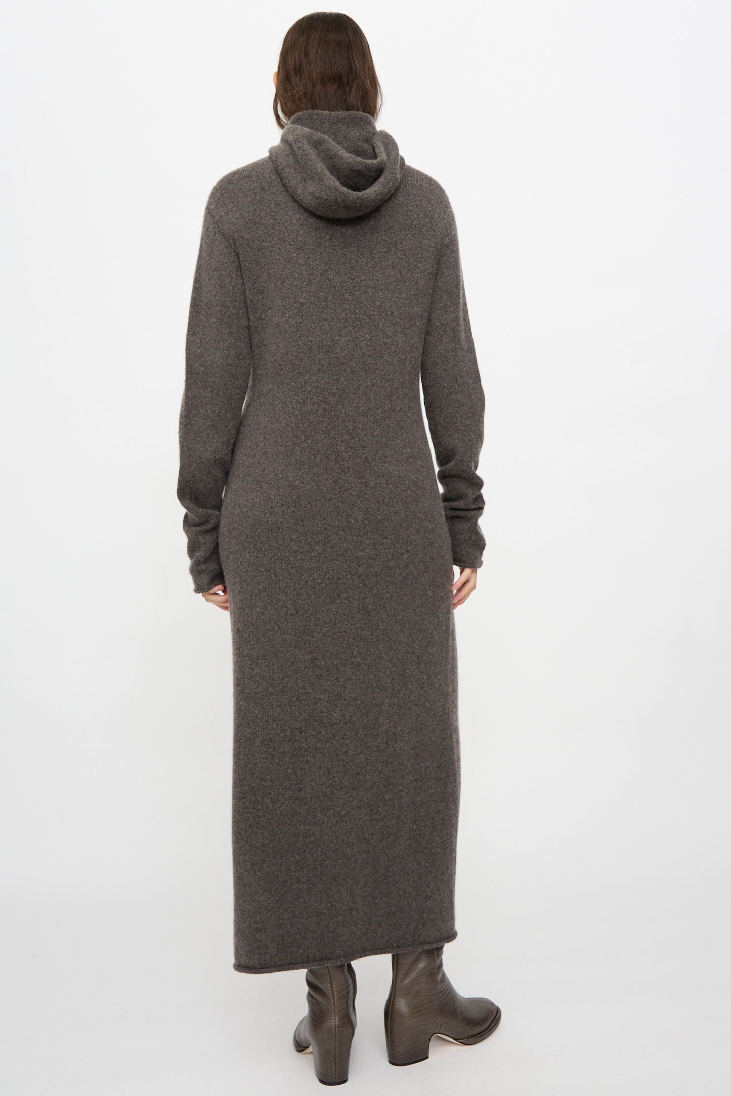A person stands with their back to the camera against a plain white background, wearing the Lauren Manoogian Soft Balaclava Dress in Blackened and brown heeled boots.