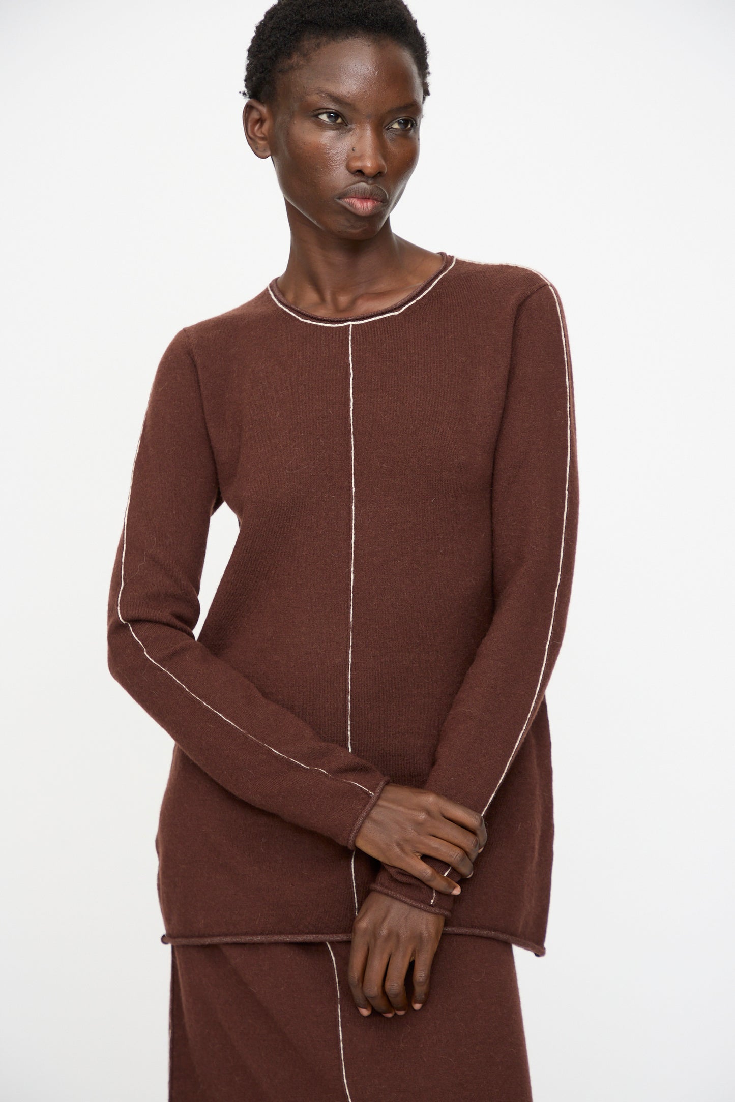 A person wears the Lauren Manoogian Stitch Crewneck in Merlot, a slim fit long sleeve top with white stitching, standing against a plain white background.