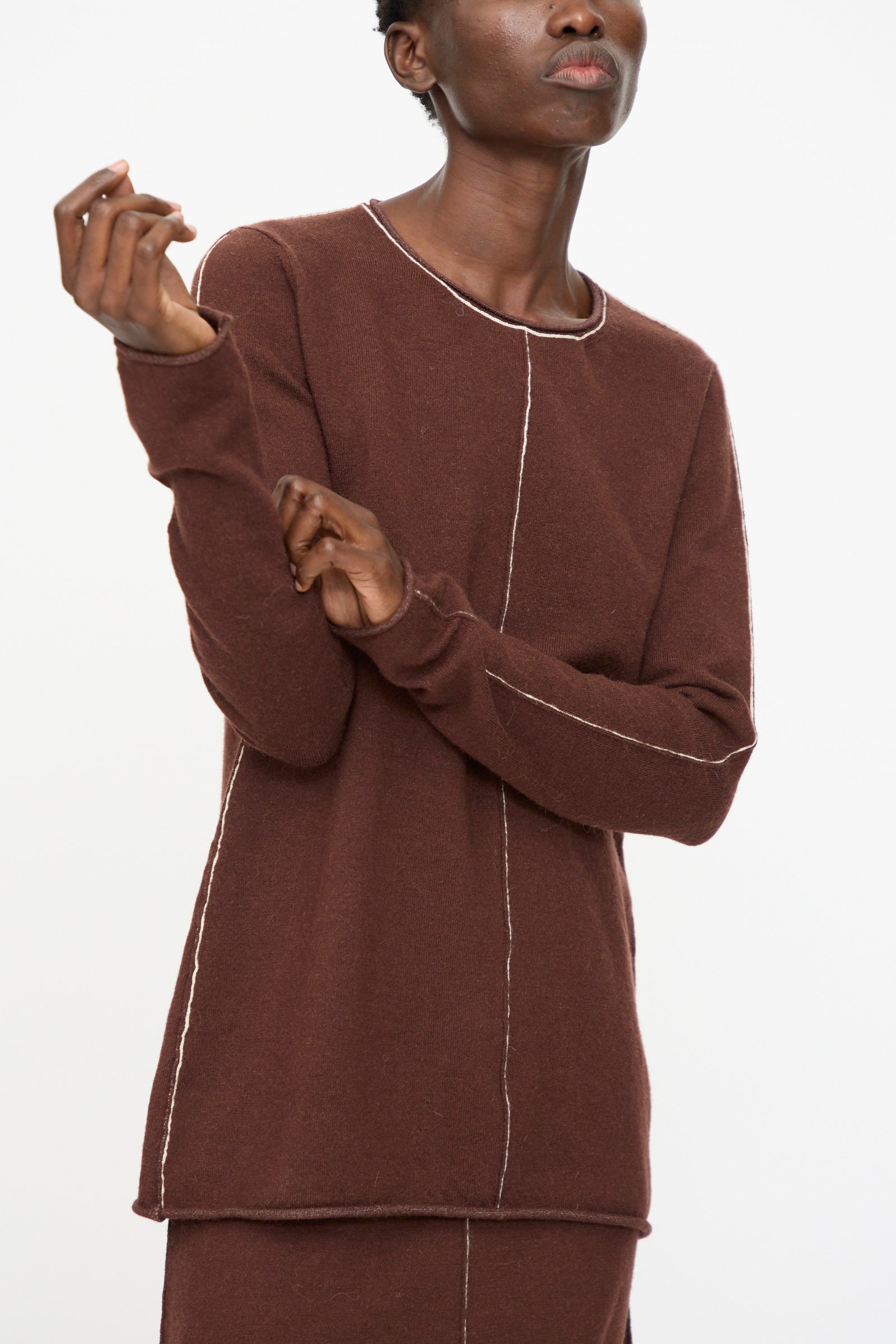 A person wearing the Lauren Manoogian Stitch Crewneck in Merlot, a slim fit long sleeve top with visible white seam detailing, stands against a plain white background.