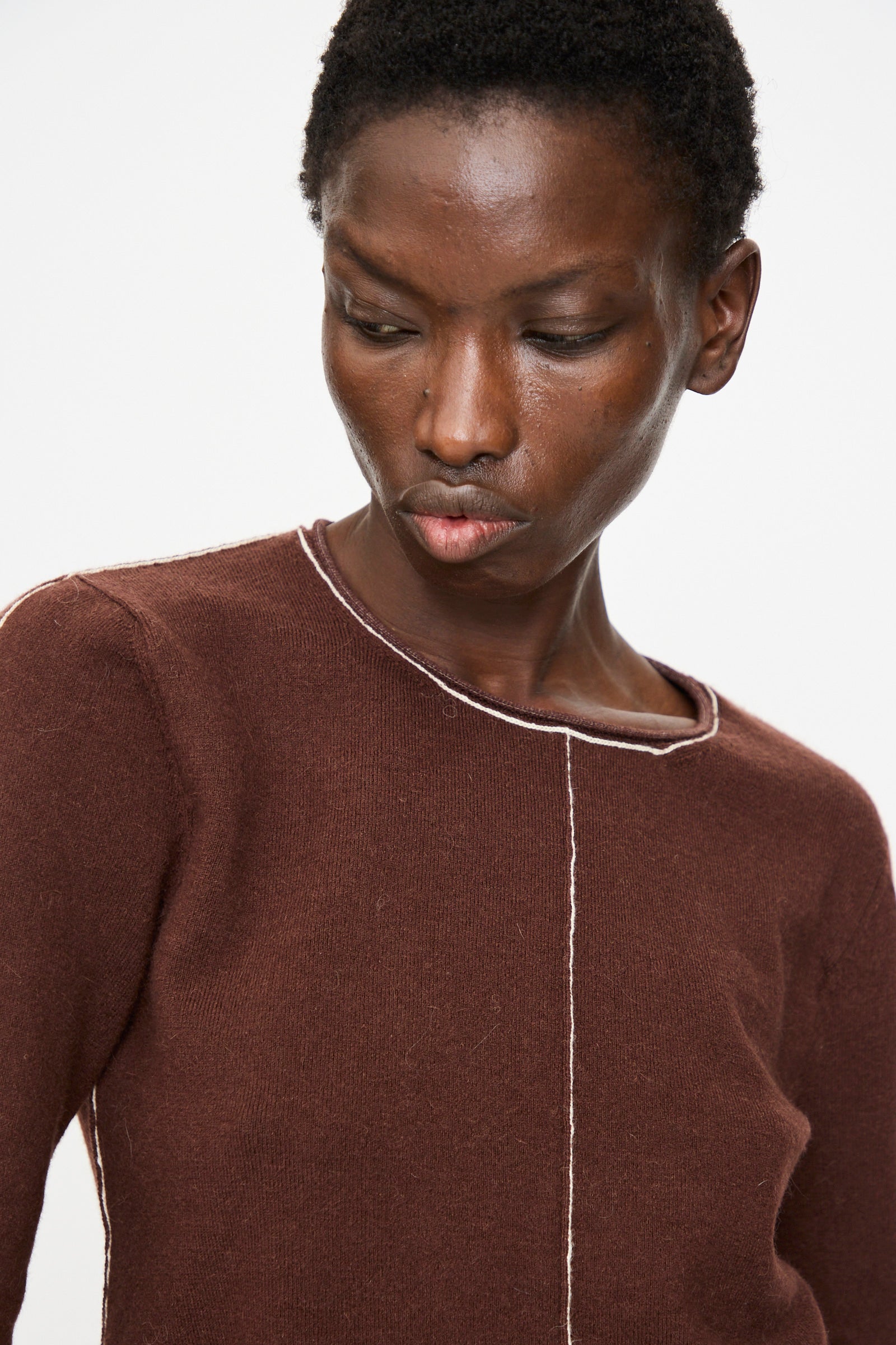 Someone wears the Lauren Manoogian Stitch Crewneck in Merlot, a slim fit long sleeve top with visible white stitching, while looking downward against a plain white background.