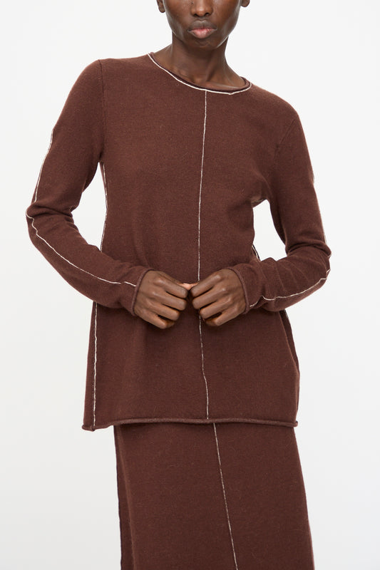 A person wearing the Lauren Manoogian Stitch Crewneck in Merlot, a slim fit long sleeve top with visible white seams, and a matching brown skirt stands against a plain white background.