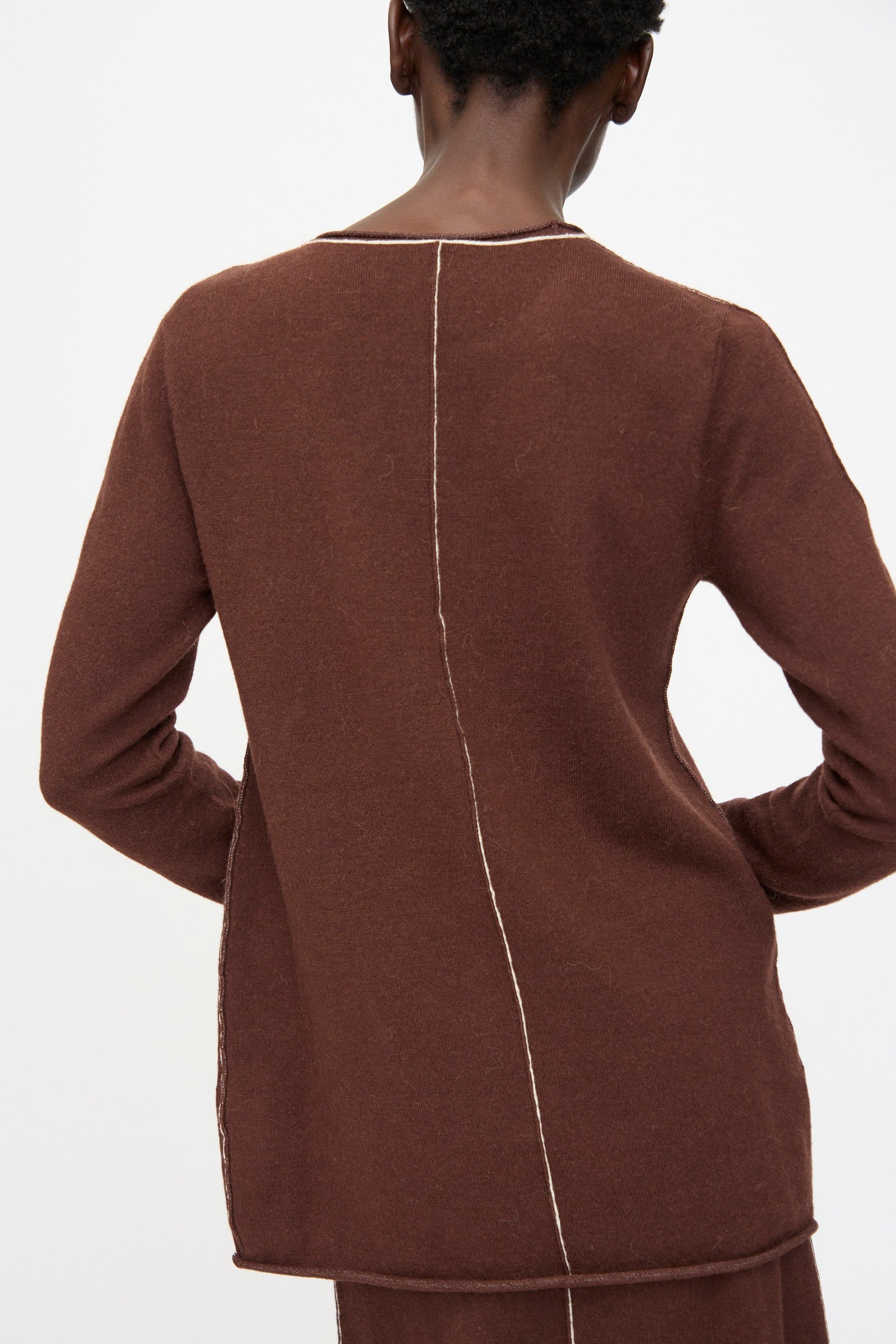 A person wears the Lauren Manoogian Stitch Crewneck in Merlot, a slim fit long sleeve top with exposed vertical seam details down the back and side, standing against a plain white background.