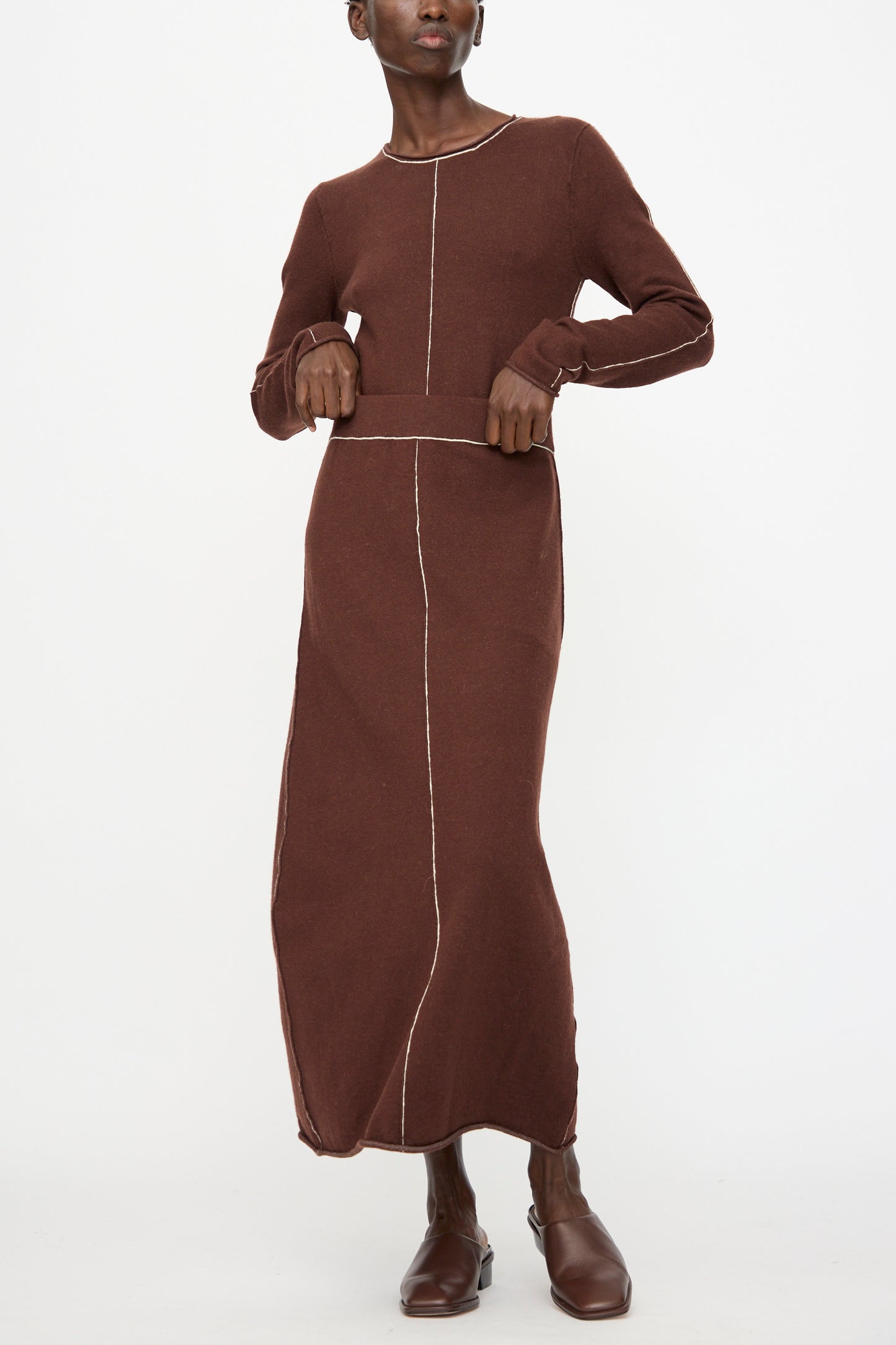 A person wearing the Lauren Manoogian Stitch Skirt in Merlot, featuring visible white stitching, stands holding the hem with both hands.