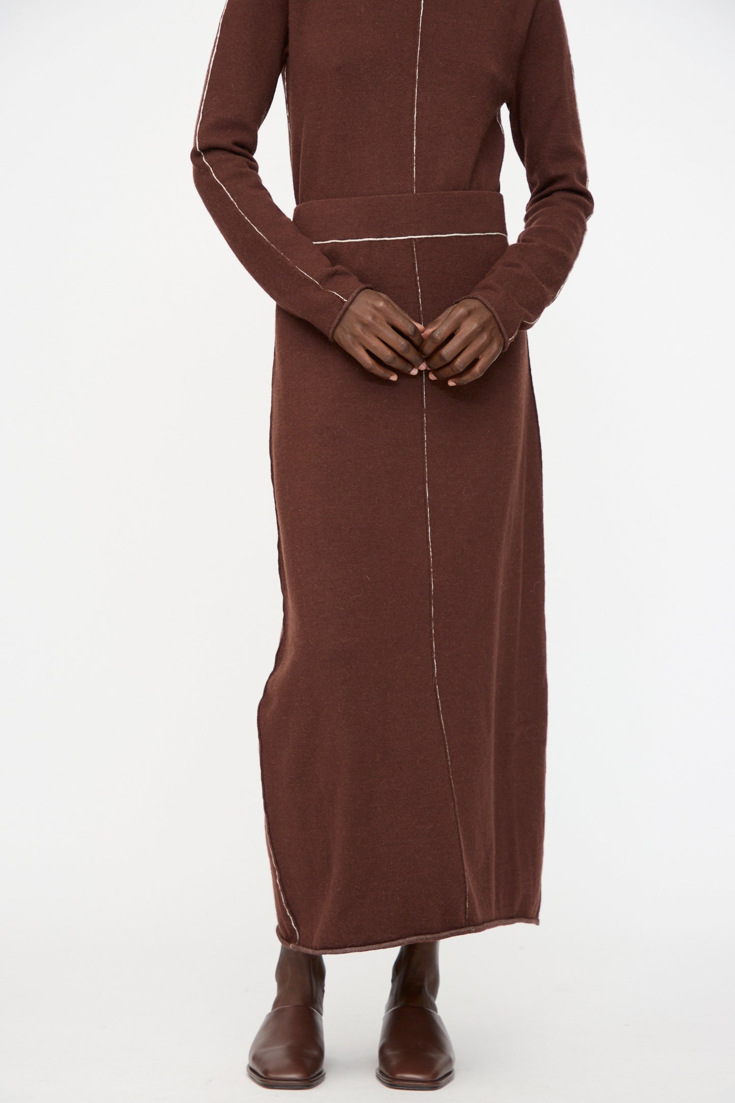 A person wearing the Lauren Manoogian Stitch Skirt in Merlot, paired with brown shoes and hands resting on the waistband.