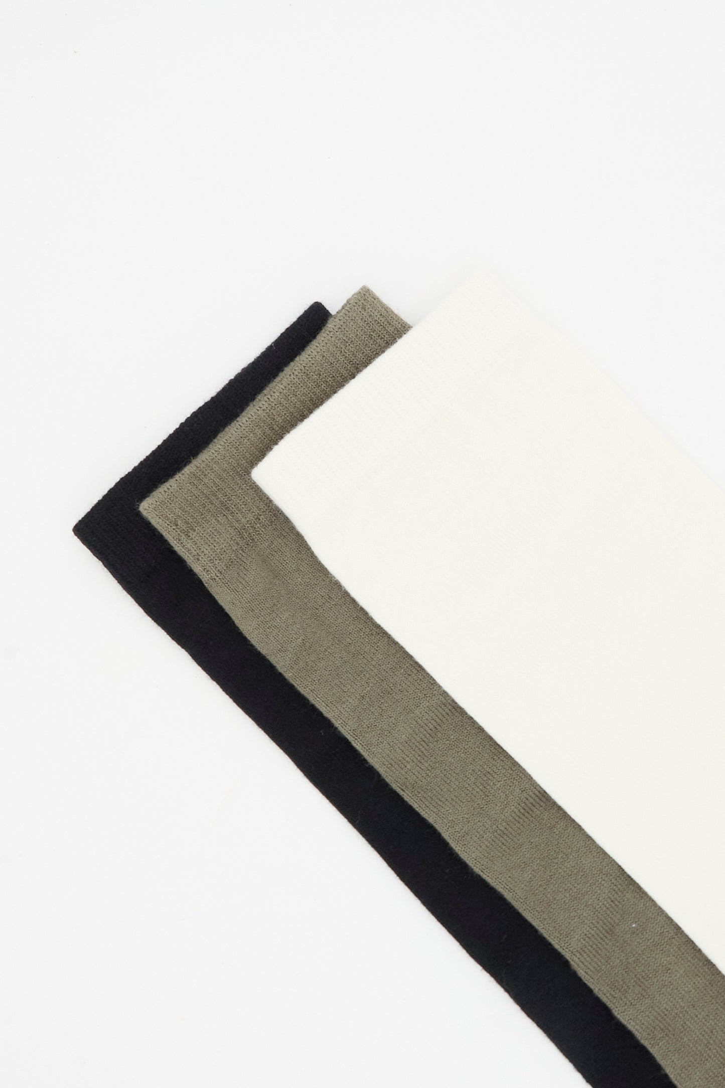 Three pairs of Tall Socks in Mix by Lauren Manoogian—black, olive green, and white—are laid out side by side on a white background. Made in Peru, these cozy alpaca wool socks offer comfort and quality craftsmanship.