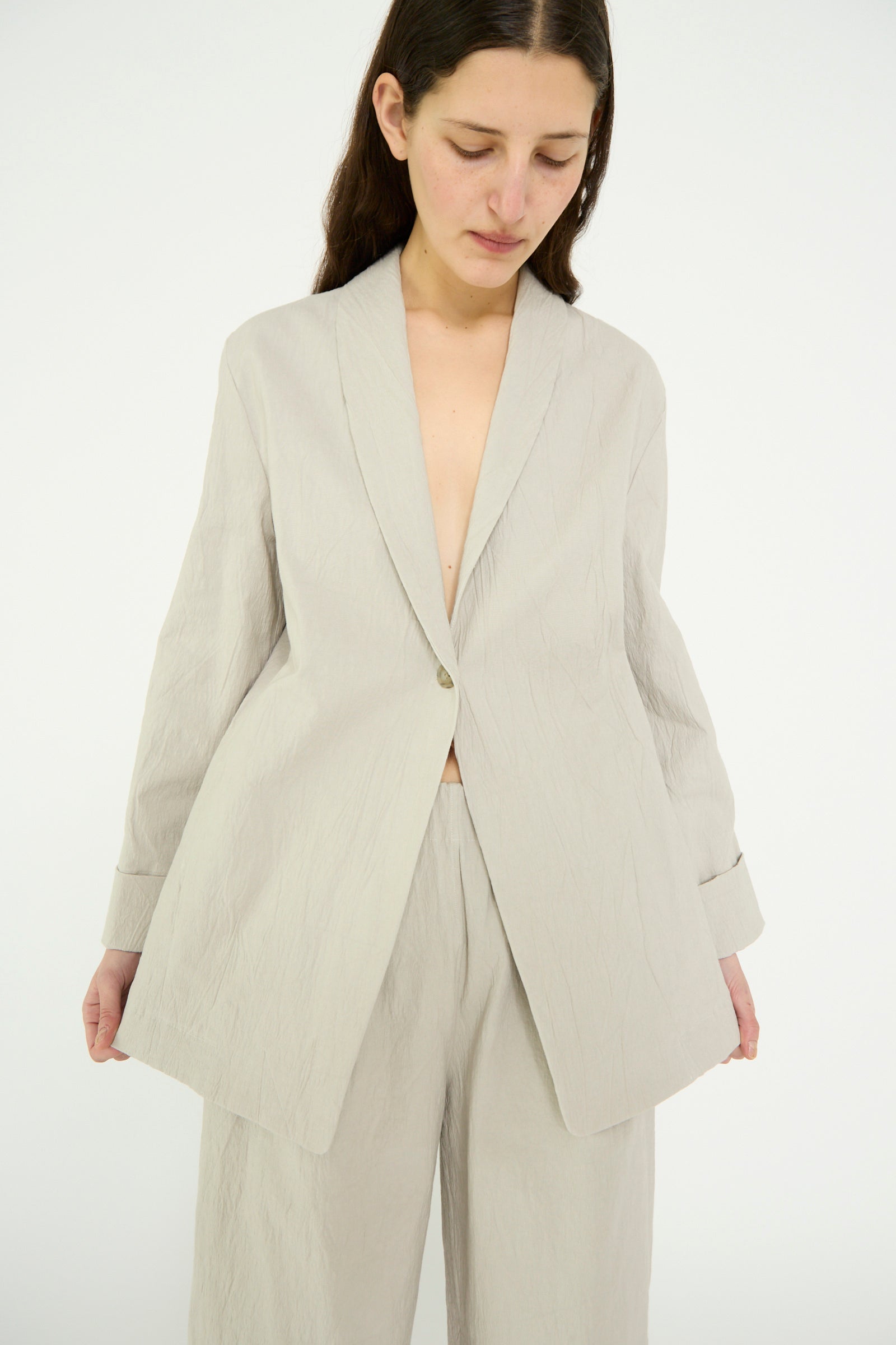 A person wears the Pewter Texture Blazer by Lauren Manoogian, featuring a loose fit, light color, single button, and oversized crinkled cotton design, against a plain backdrop.