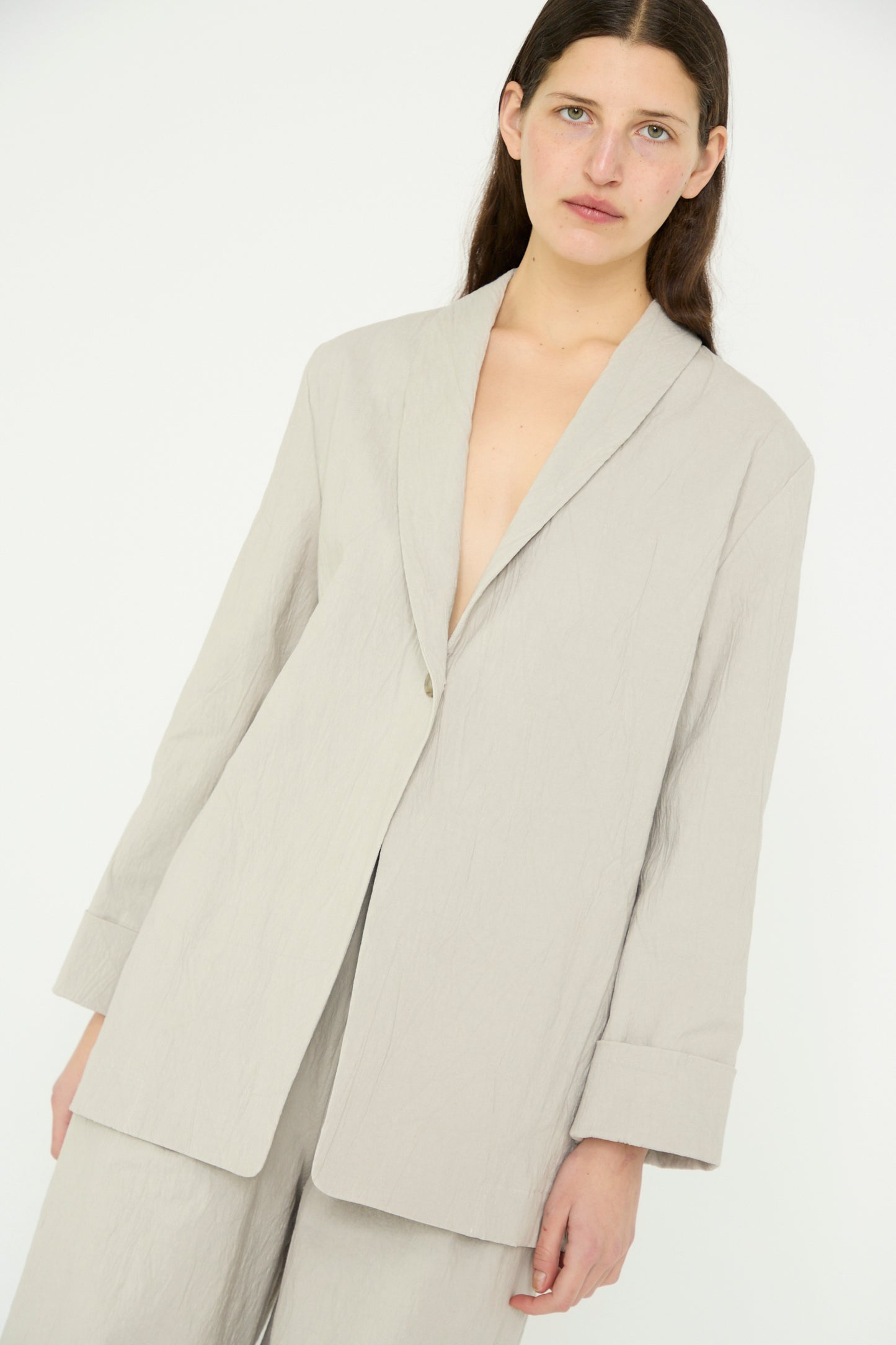 A person stands against a plain background, wearing the Texture Blazer in Pewter by Lauren Manoogian with a shawl collar and matching pants, looking forward.