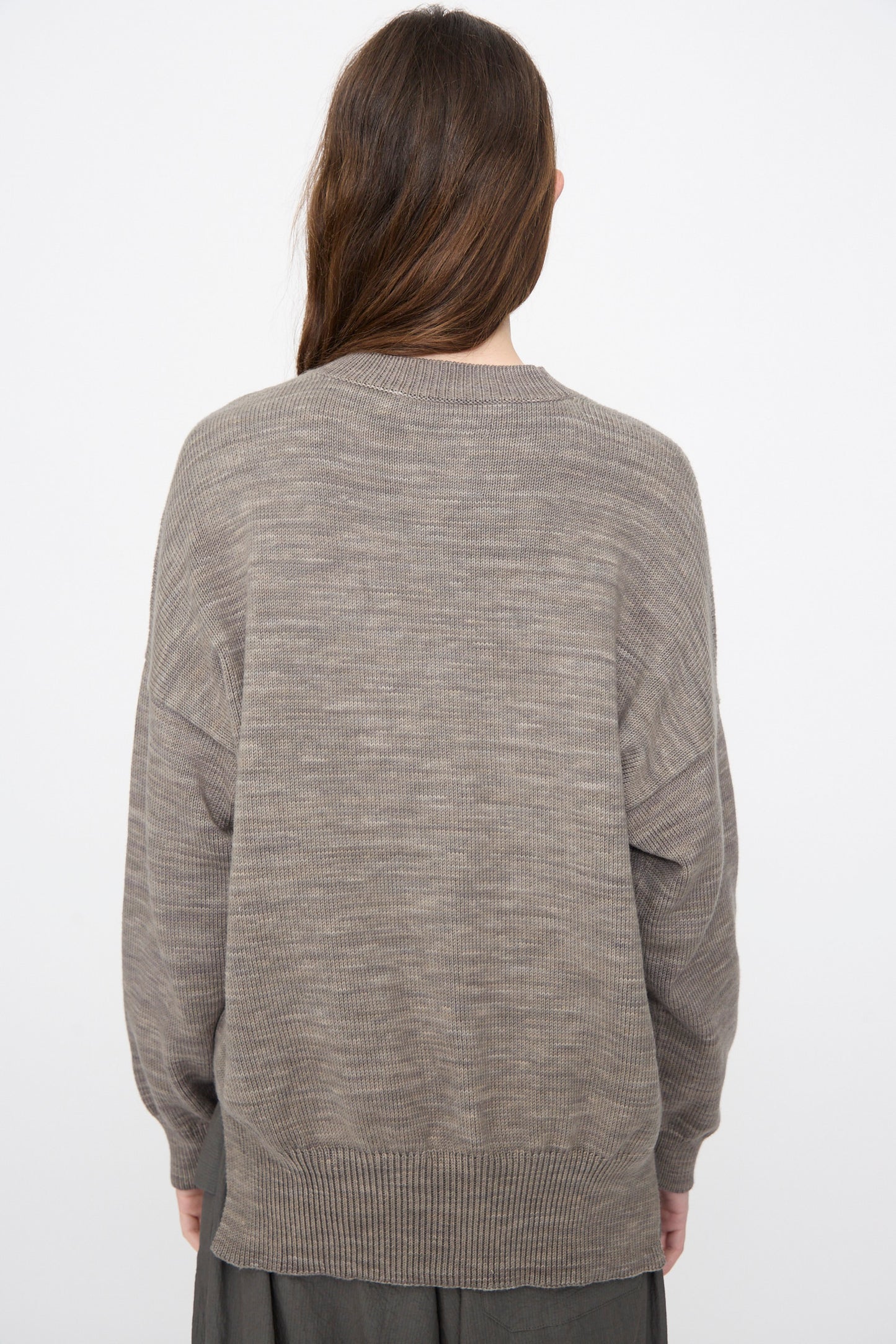 A person with long brown hair is seen from behind wearing the Lauren Manoogian Watercolor Crewneck in Rock, styled with a dark skirt, set against a plain white background.