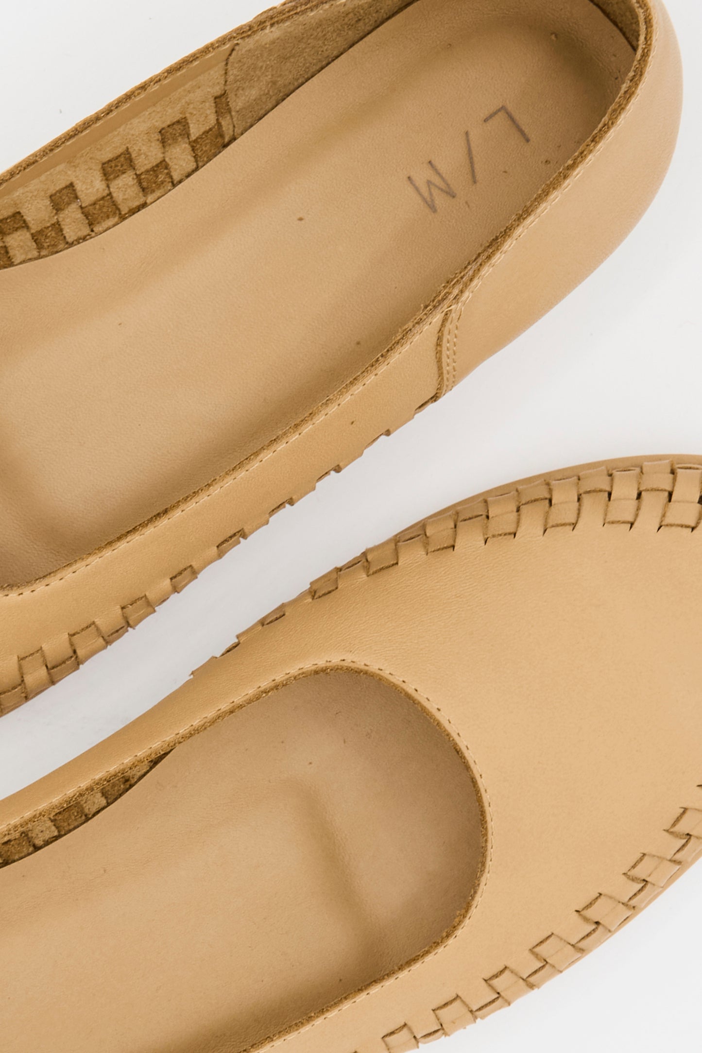 Close-up of Lauren Manoogian’s Weave Shoe in Natural: two tan leather slip-ons with visible stitching, a woven rim detail, and "L/M" printed on the insole.