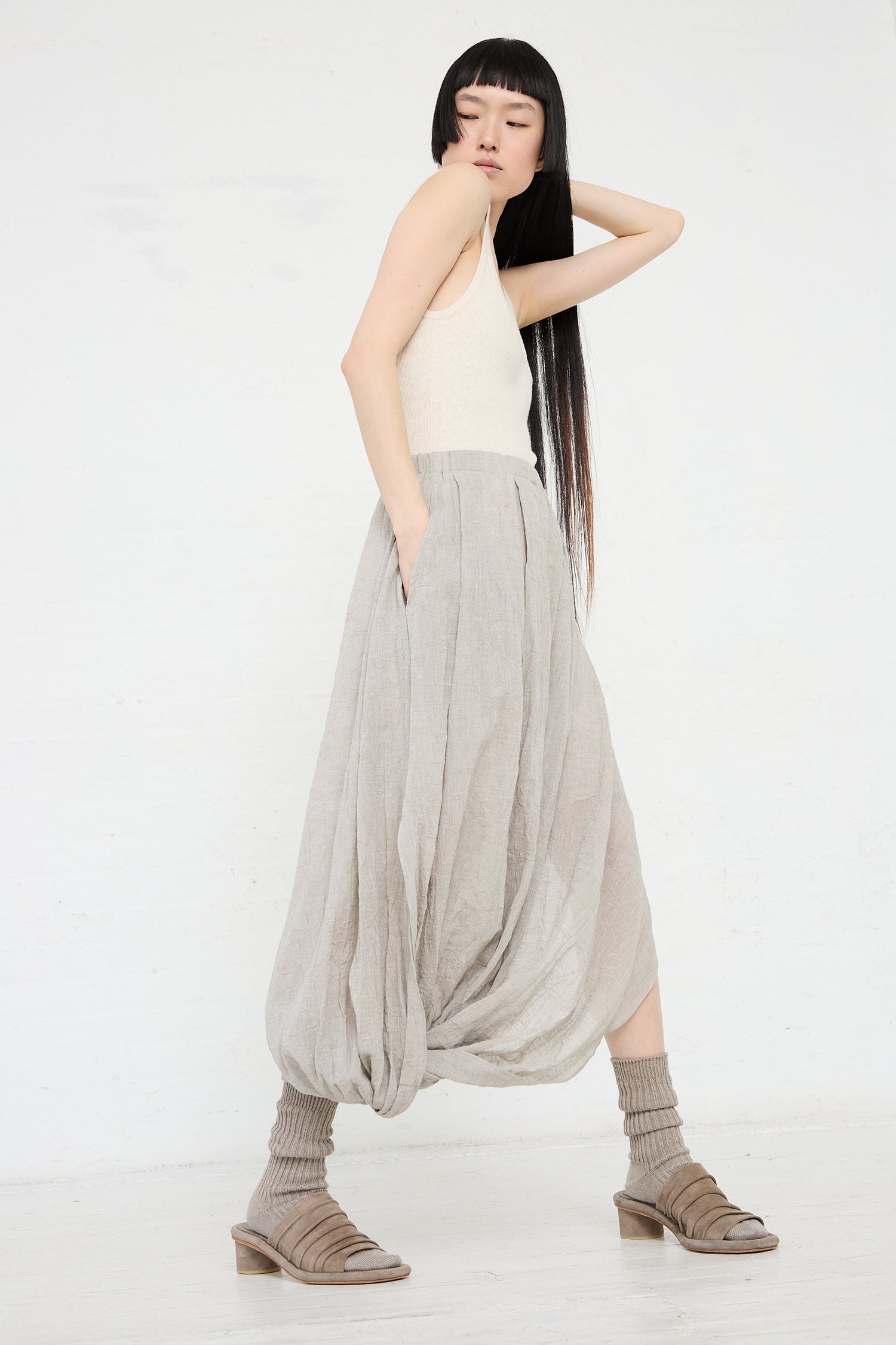 A woman in a beige cotton/linen blend top and Lauren Manoogian's Gauze Twist Skirt in Ash poses against a white background, her arm resting on her head.