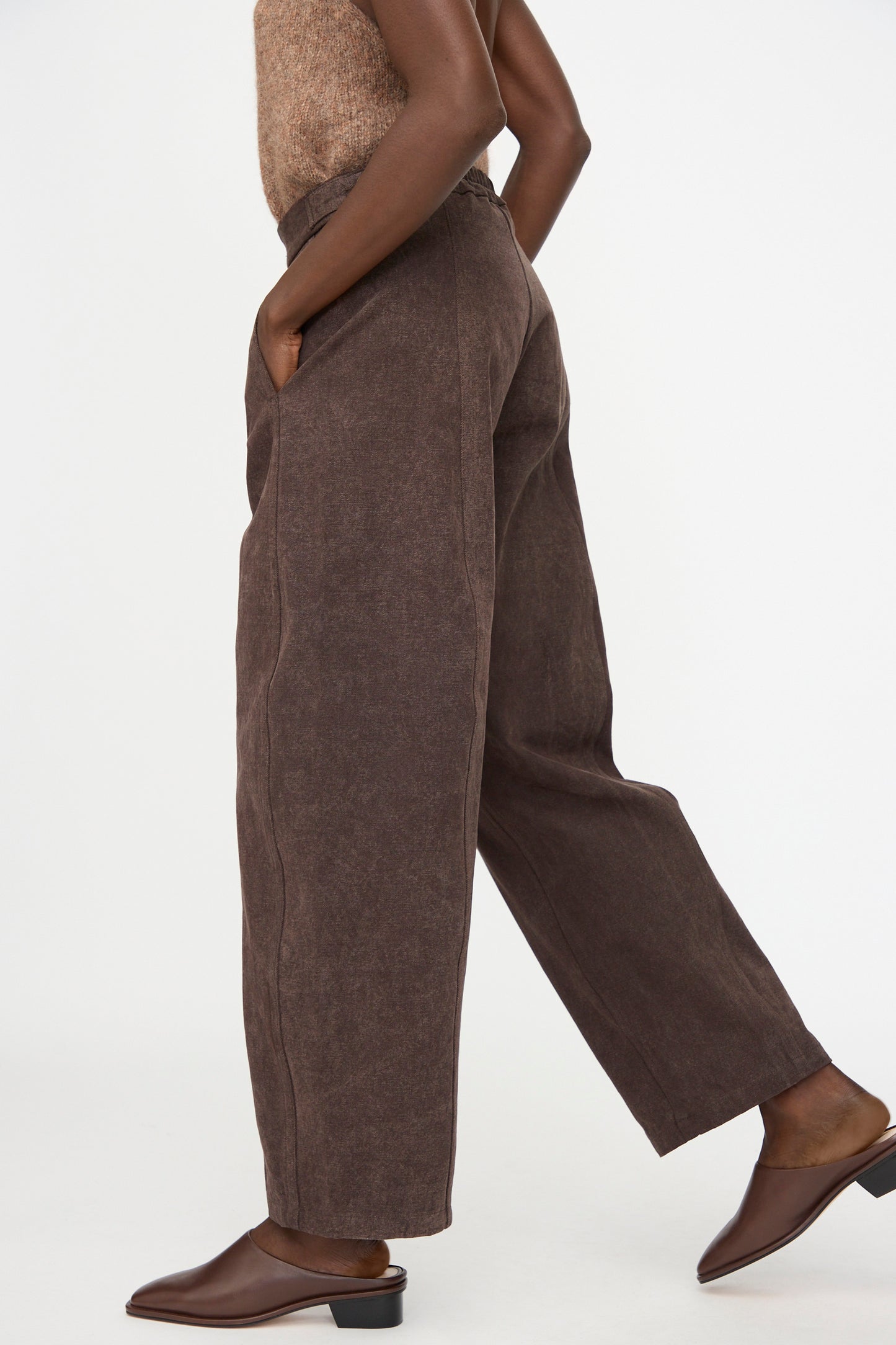 A person wearing Lauren Manoogian's Canvas Pants in Washed Soil, a sleeveless top, and brown slip-on shoes stands with one leg slightly forward against a plain white background.