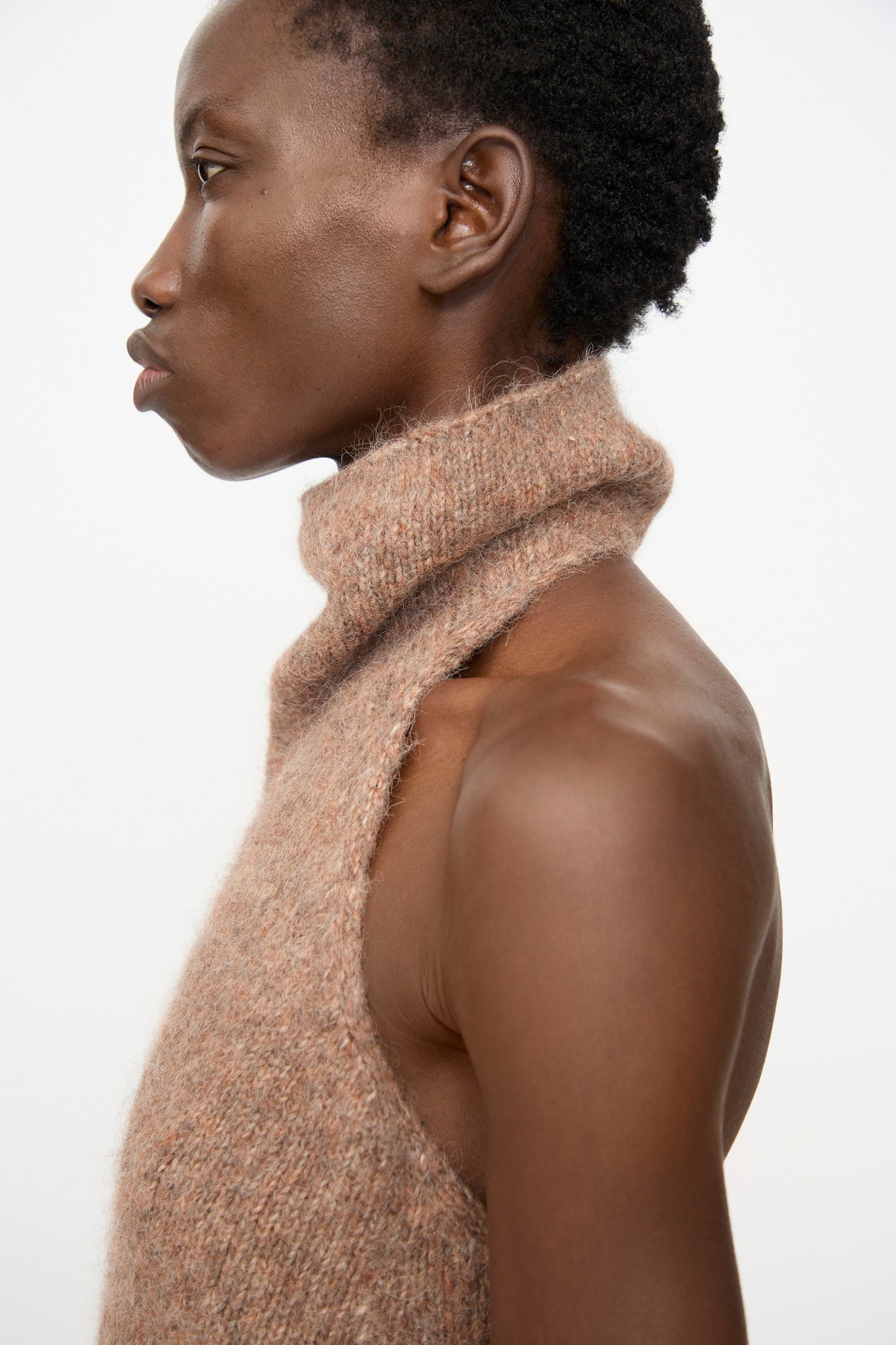 A person in profile wears the Lauren Manoogian Loft Halter in Spice, a sleeveless suri alpaca blend knit top with a high neck, set against a plain white background.