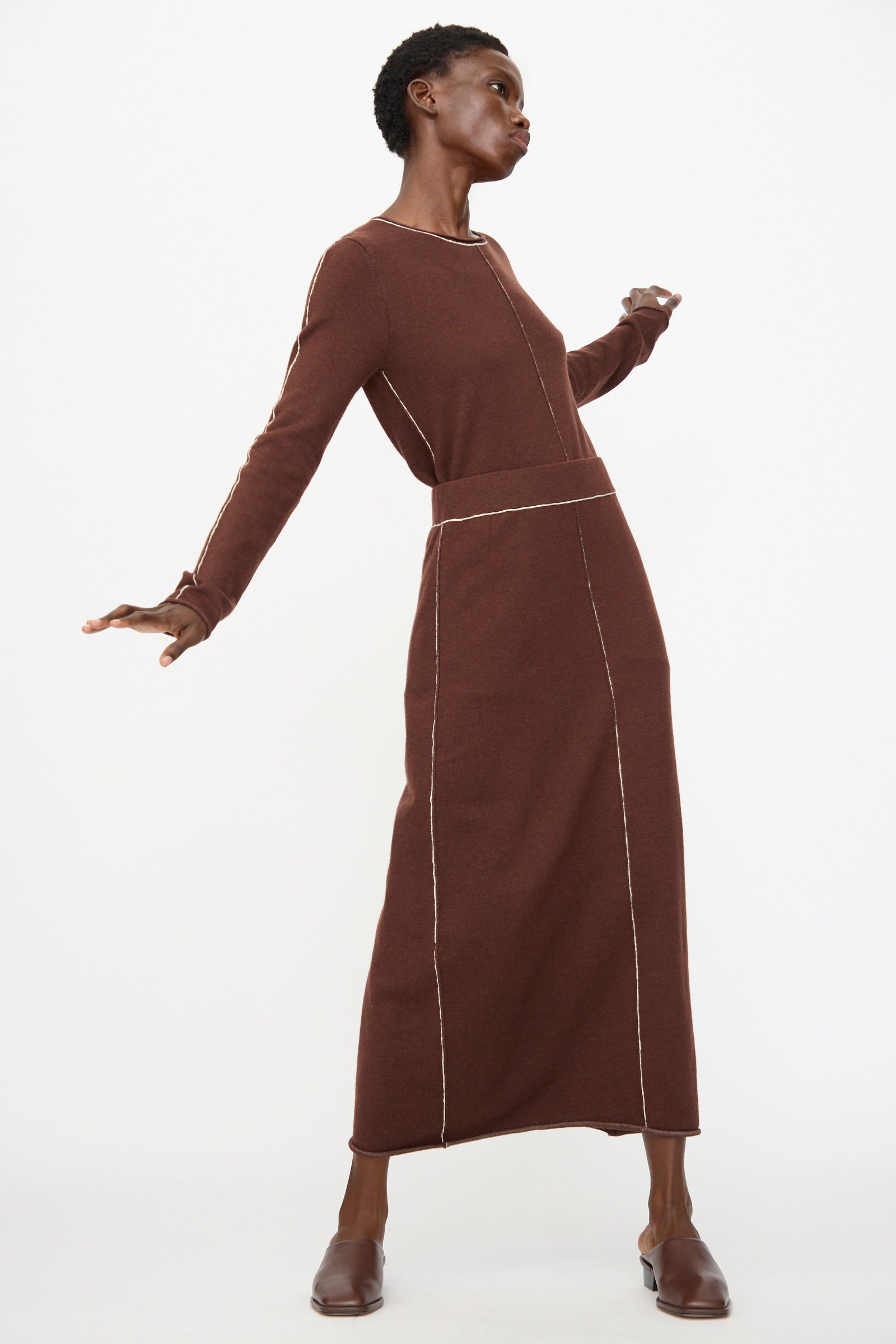 Model wears the Lauren Manoogian Stitch Skirt in Merlot, an ankle-length, long-sleeved design with visible seam lines, posing dynamically against a plain white background.