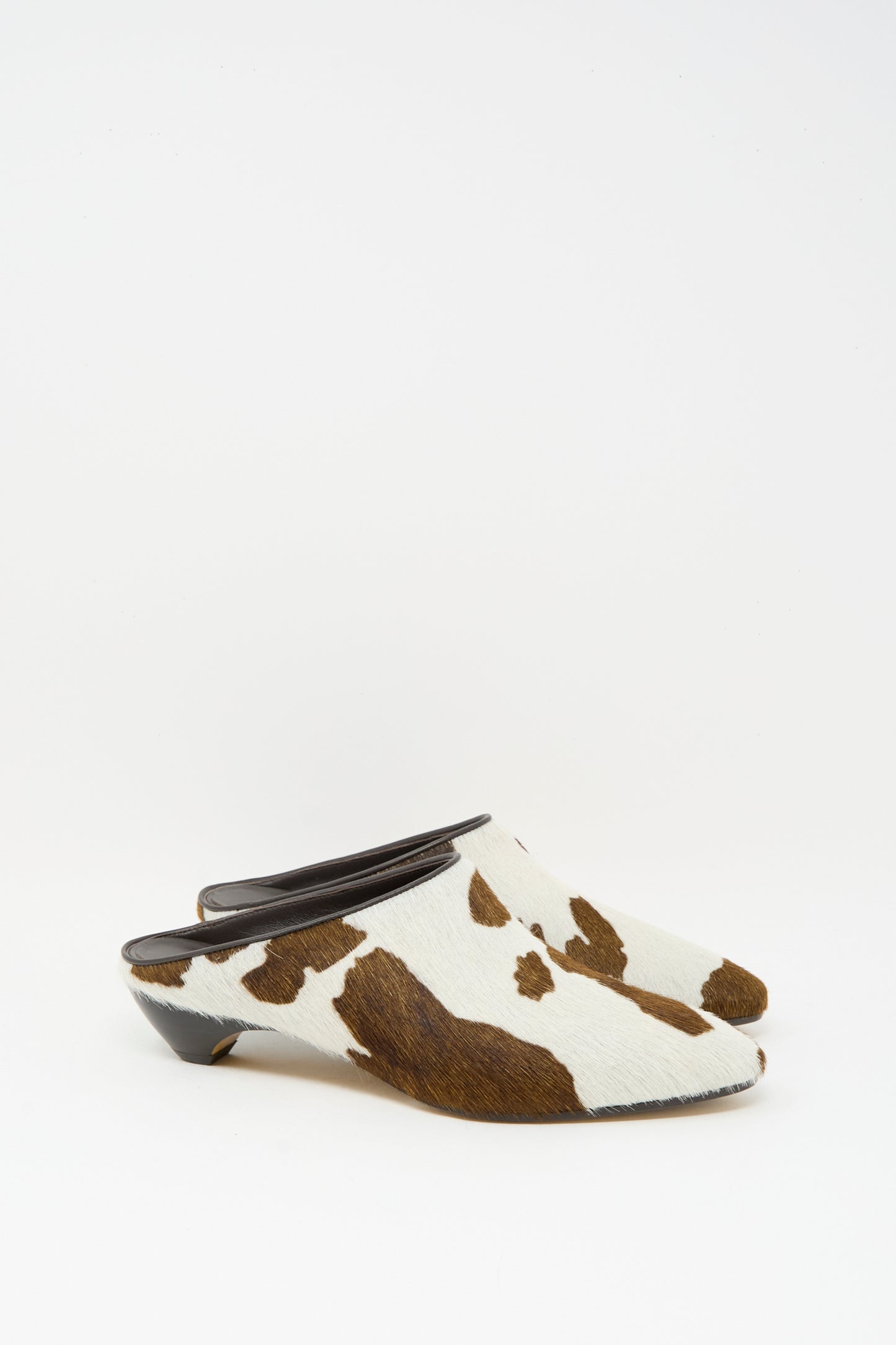 The Le Monde Beryl Allegra Mule in Cow features a low mini heel and calf hair leather upper with a chic brown and white cow print, displayed on a white background.
