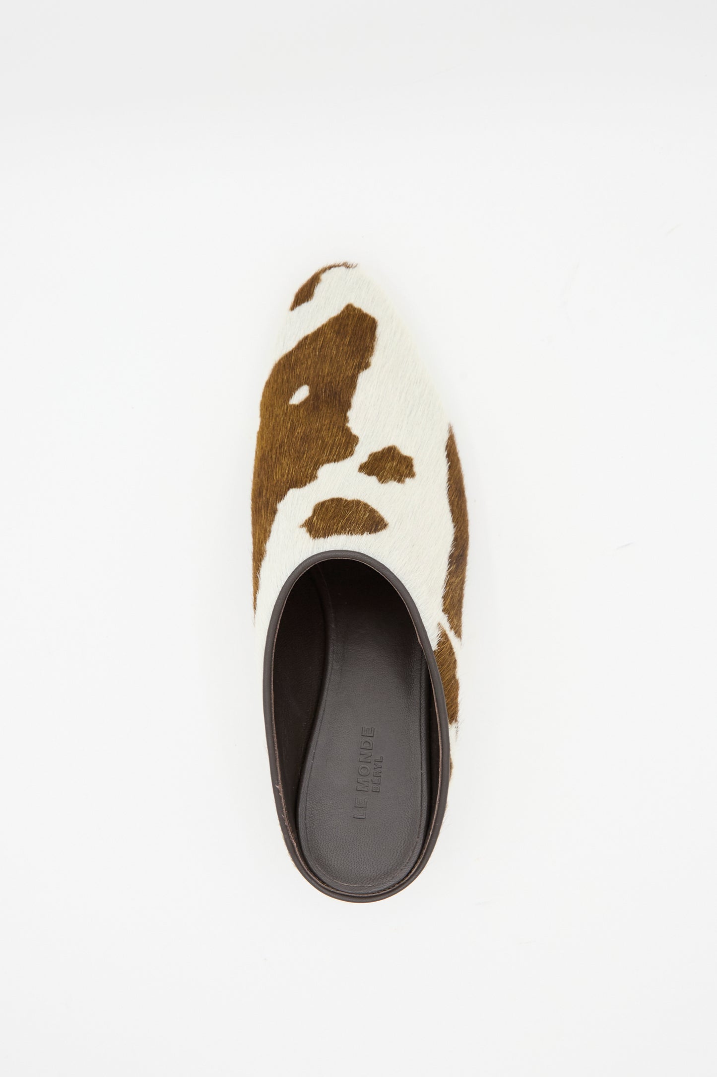 The Allegra Mule in Cow by Le Monde Beryl—a mini heeled mule crafted from calf hair leather with a brown and white cow print—is shown from above on a plain white background.