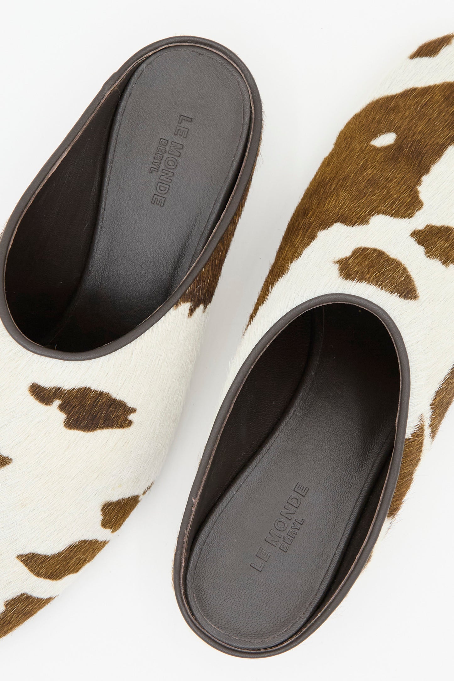 The Allegra Mule in Cow by Le Monde Beryl features brown and white cow print calf hair leather uppers, black insoles, and a slip-on mini heel design.