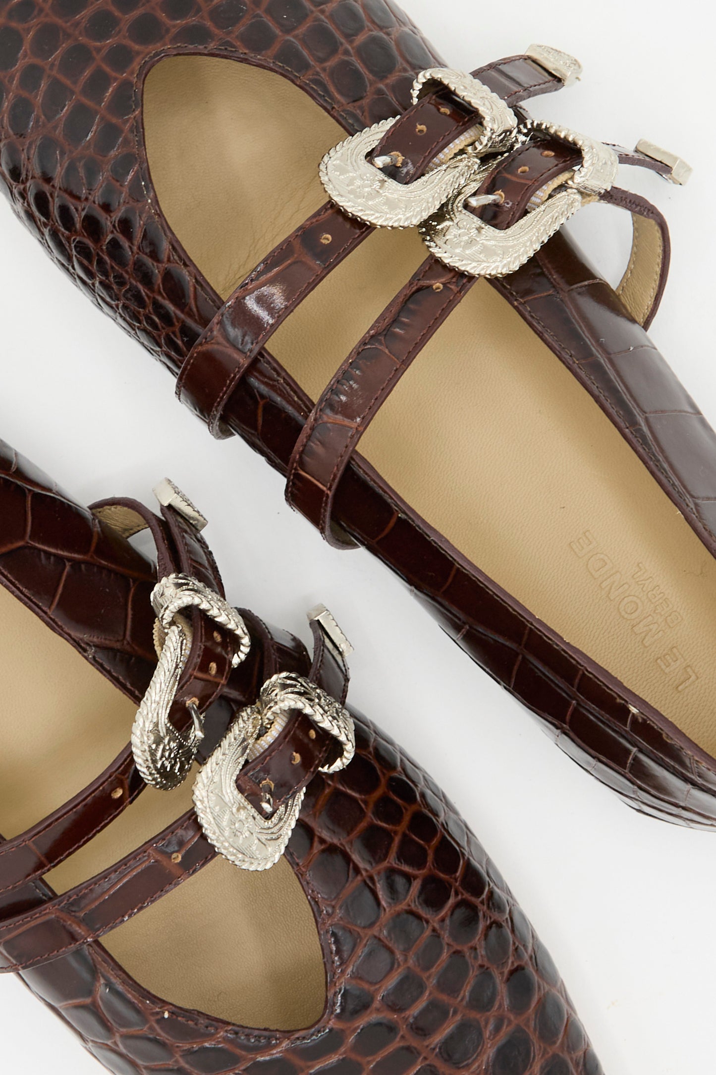 Close-up of Le Monde Beryl’s Claudia Slipper in Coco Brown, featuring crocodile-patterned calf leather, double silver buckles, and beige insoles. Made in Italy and displayed on a white background.
