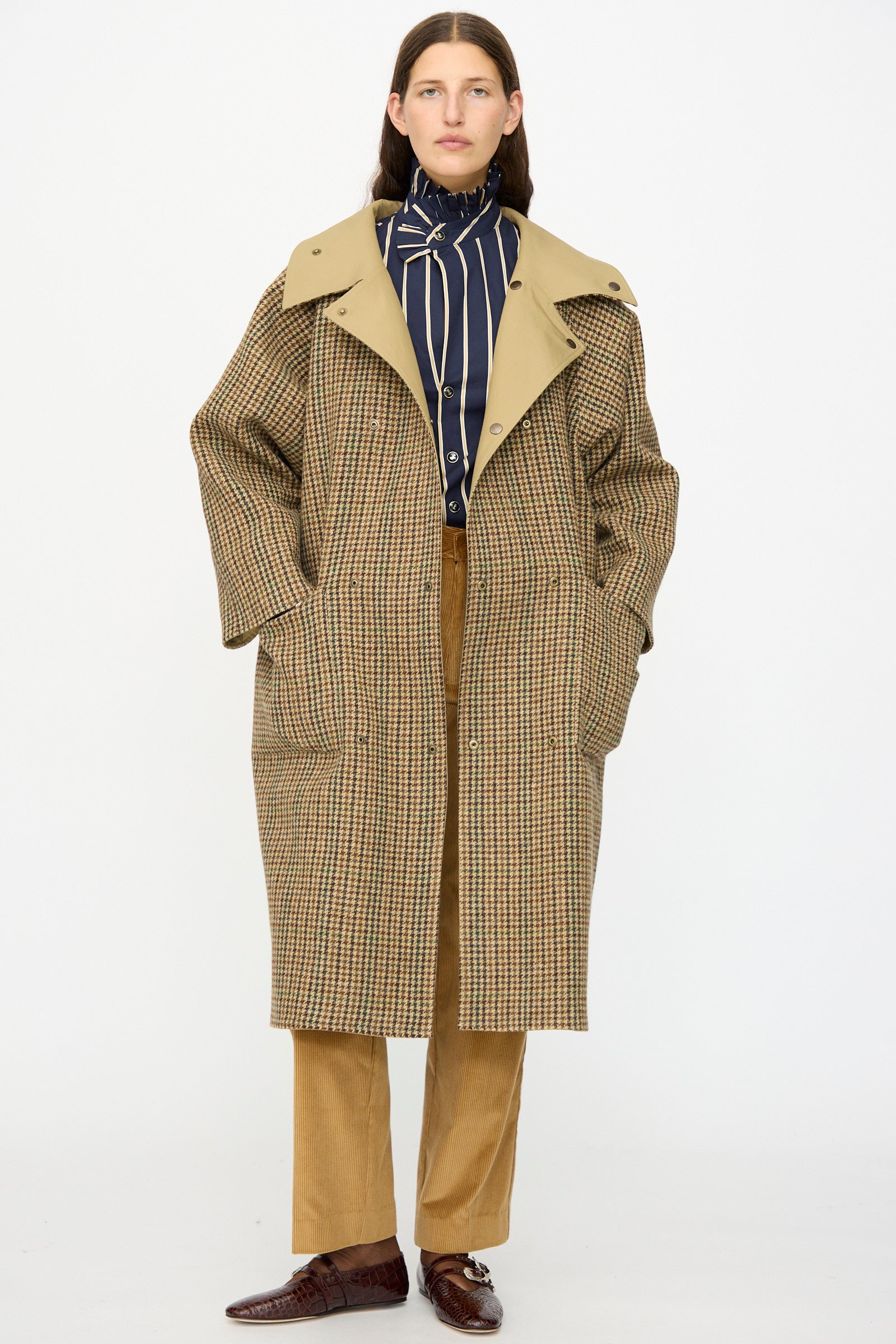 Model wears the Les Prairies De Paris Dickens Moon Reversible British Trench in Taupe over a striped shirt and tan pants with brown shoes, standing against a plain white background.